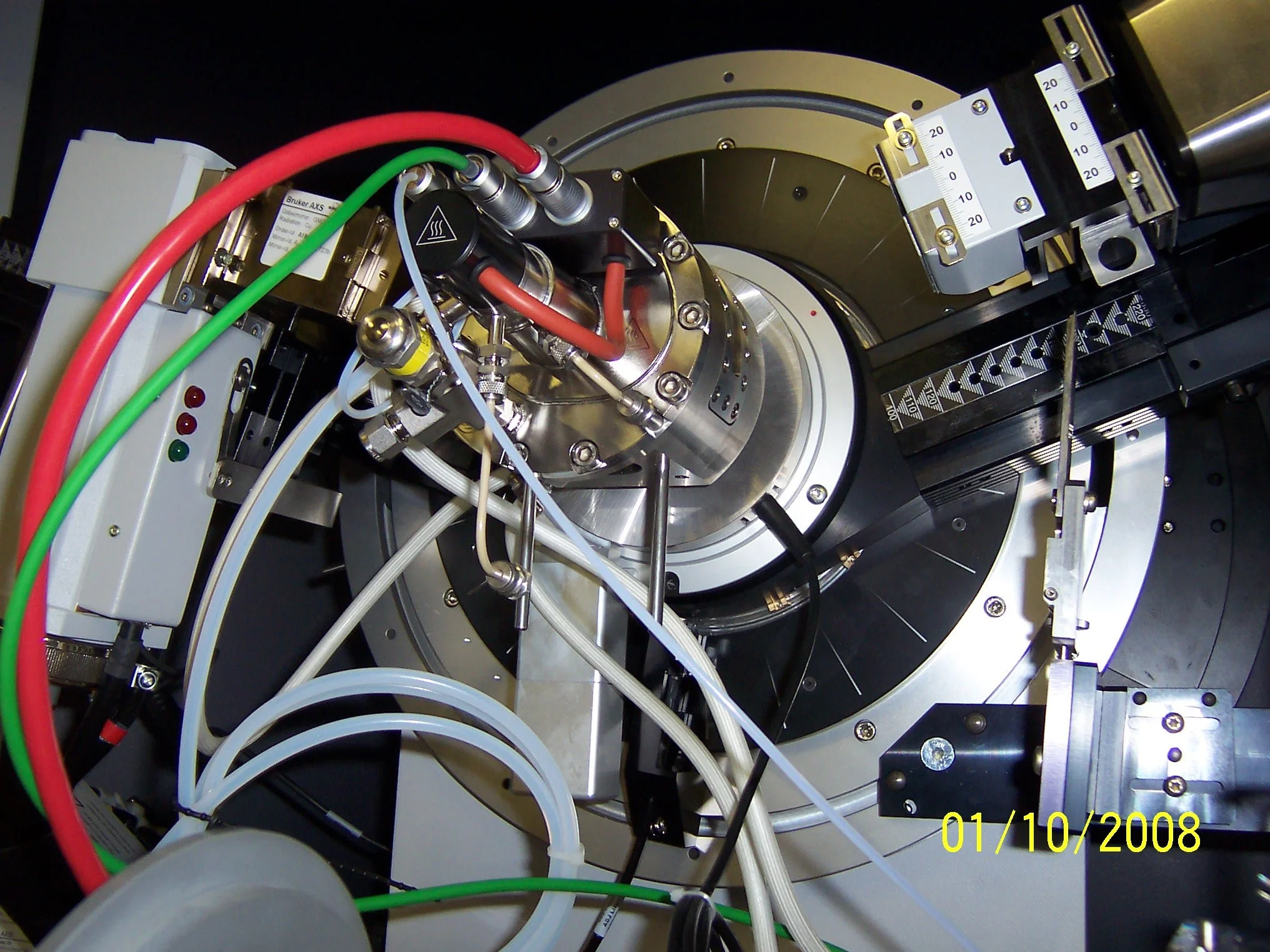 Close-up view of a complex scientific laboratory instrument with various tubes, wires, and metallic components. The date '01/10/2008' is displayed in yellow at the bottom right corner.