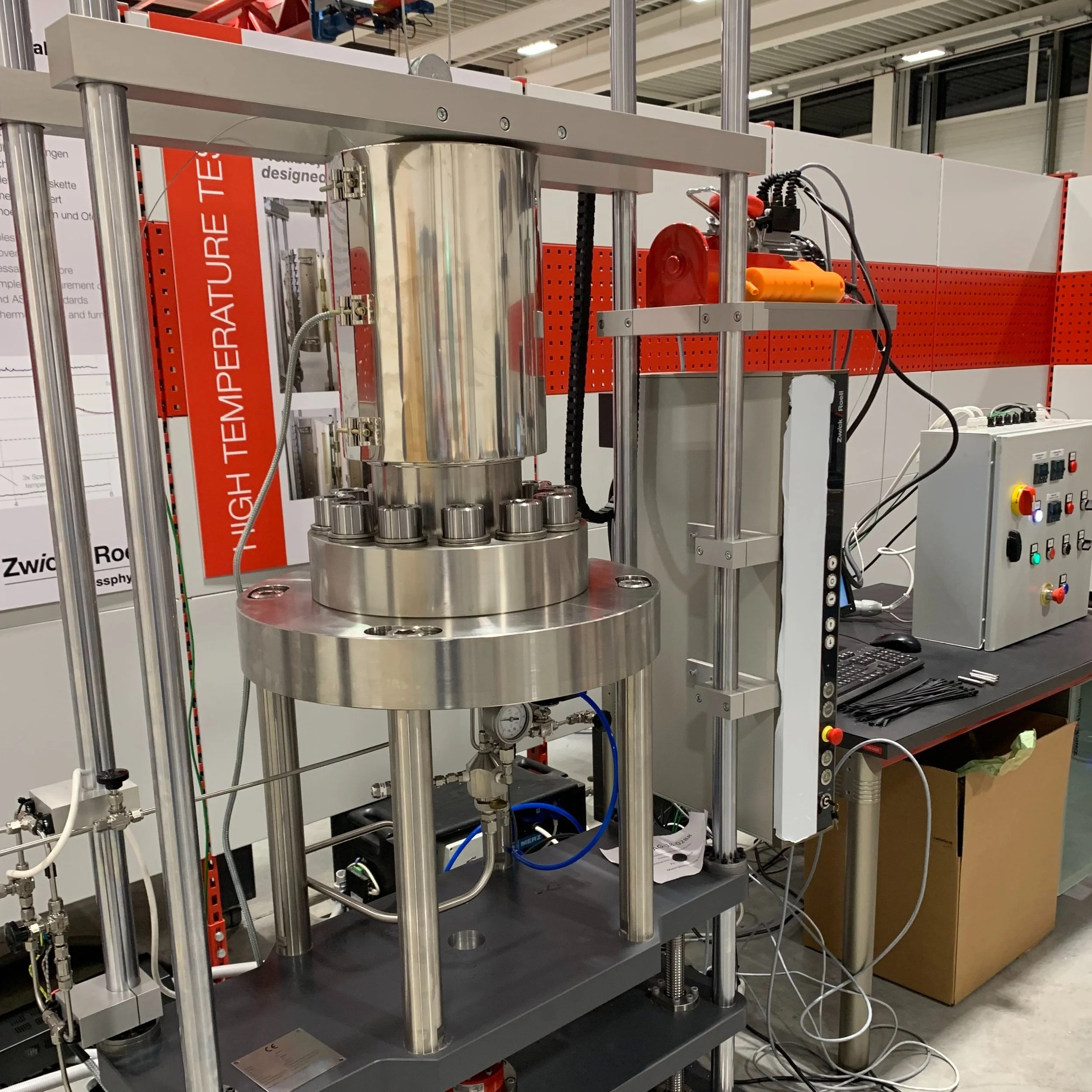 A scientific experimental setup with metal framework, cylindrical chamber, gauges, valves, wires, and control panel in a laboratory setting.