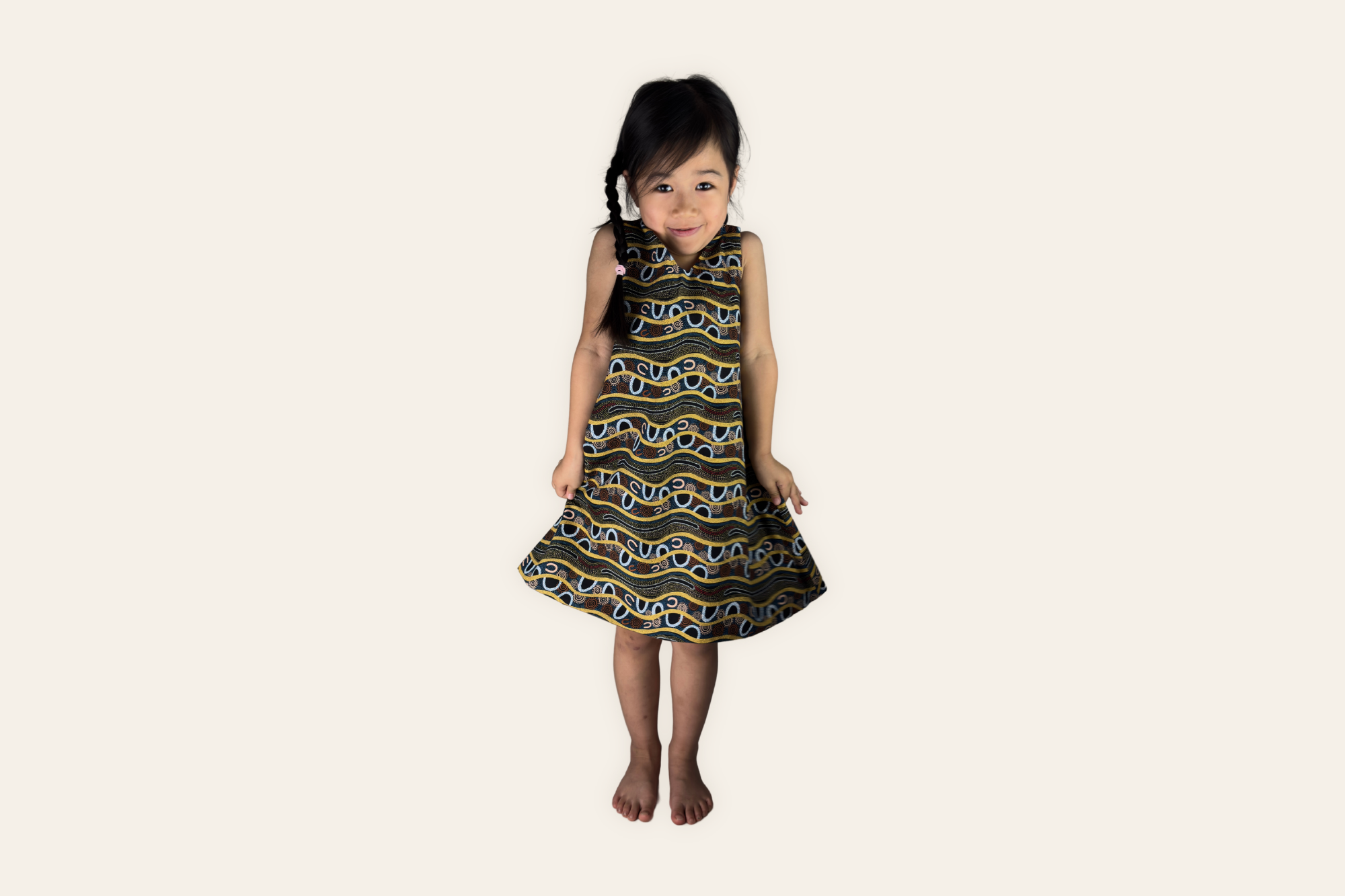 Young girl wearing a WMB STUDIO reversible Penefold dress in certified Aboriginal artwork fabric on a soft cream background.