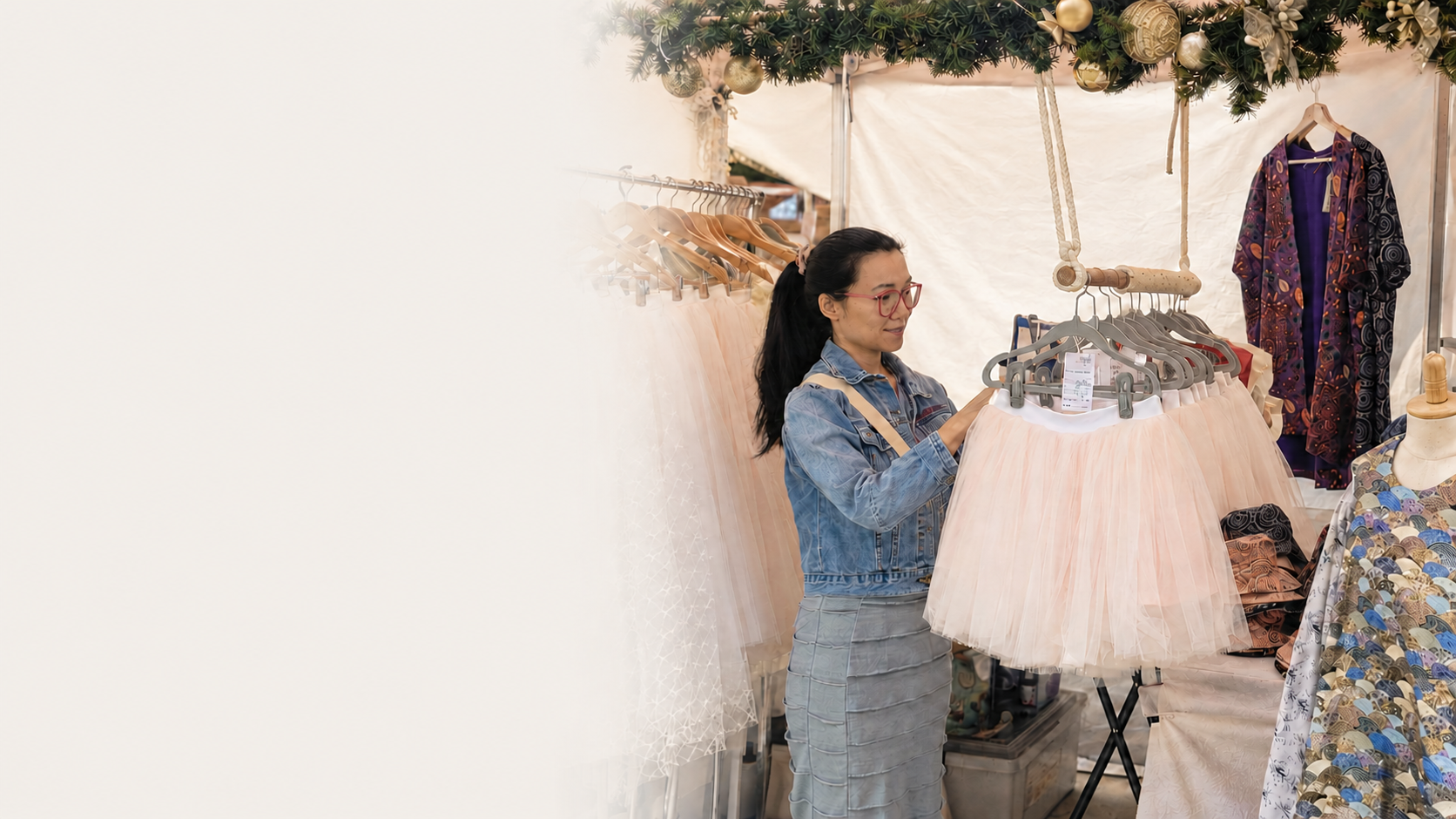 Catherine Yang arranging blush tulle skirts at her market stall, with handmade clothing and a reversible Penefold on display.