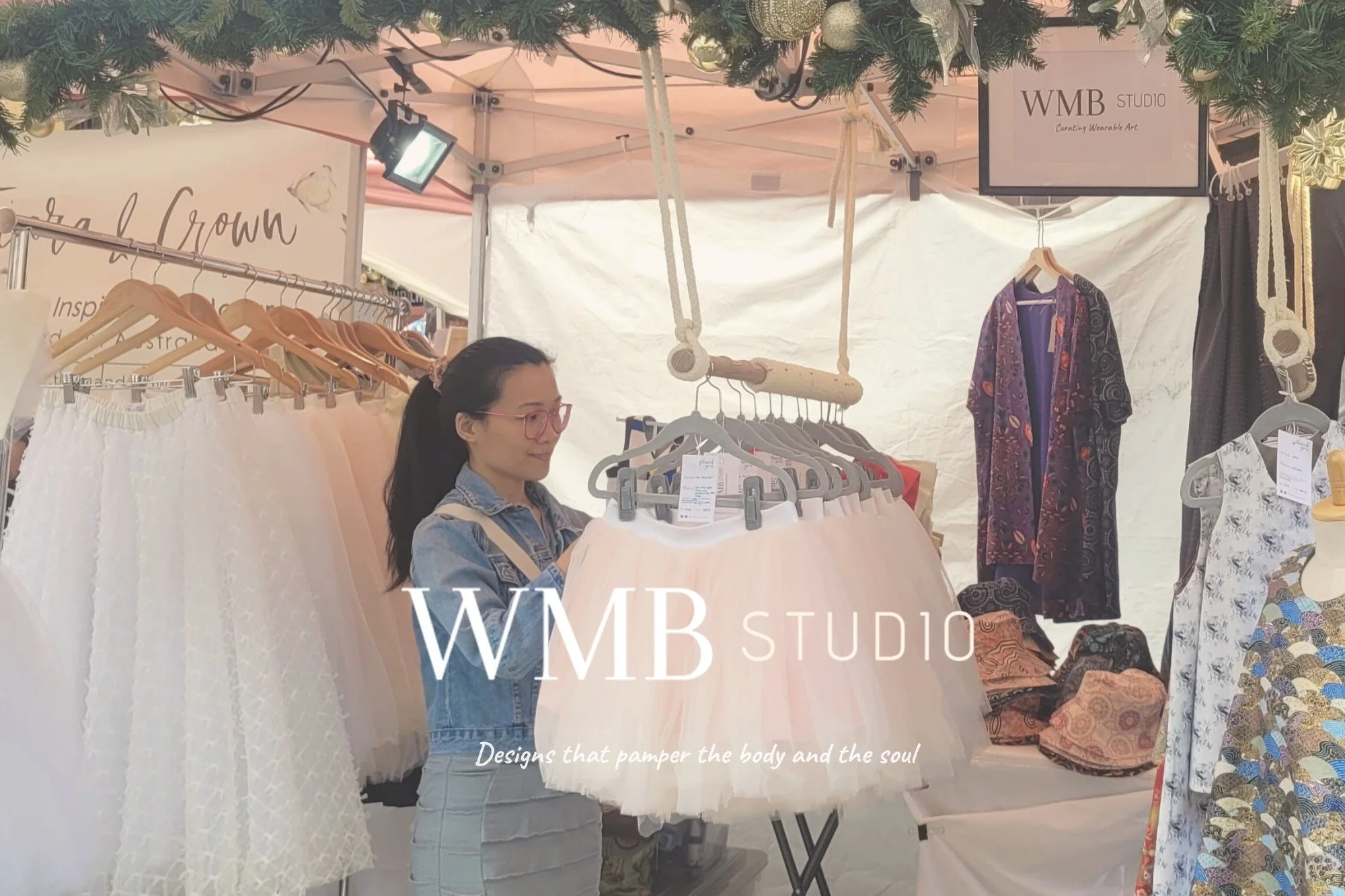 Catherine Yang standing at the WMB Studio market stall surrounded by handmade skirts and hats