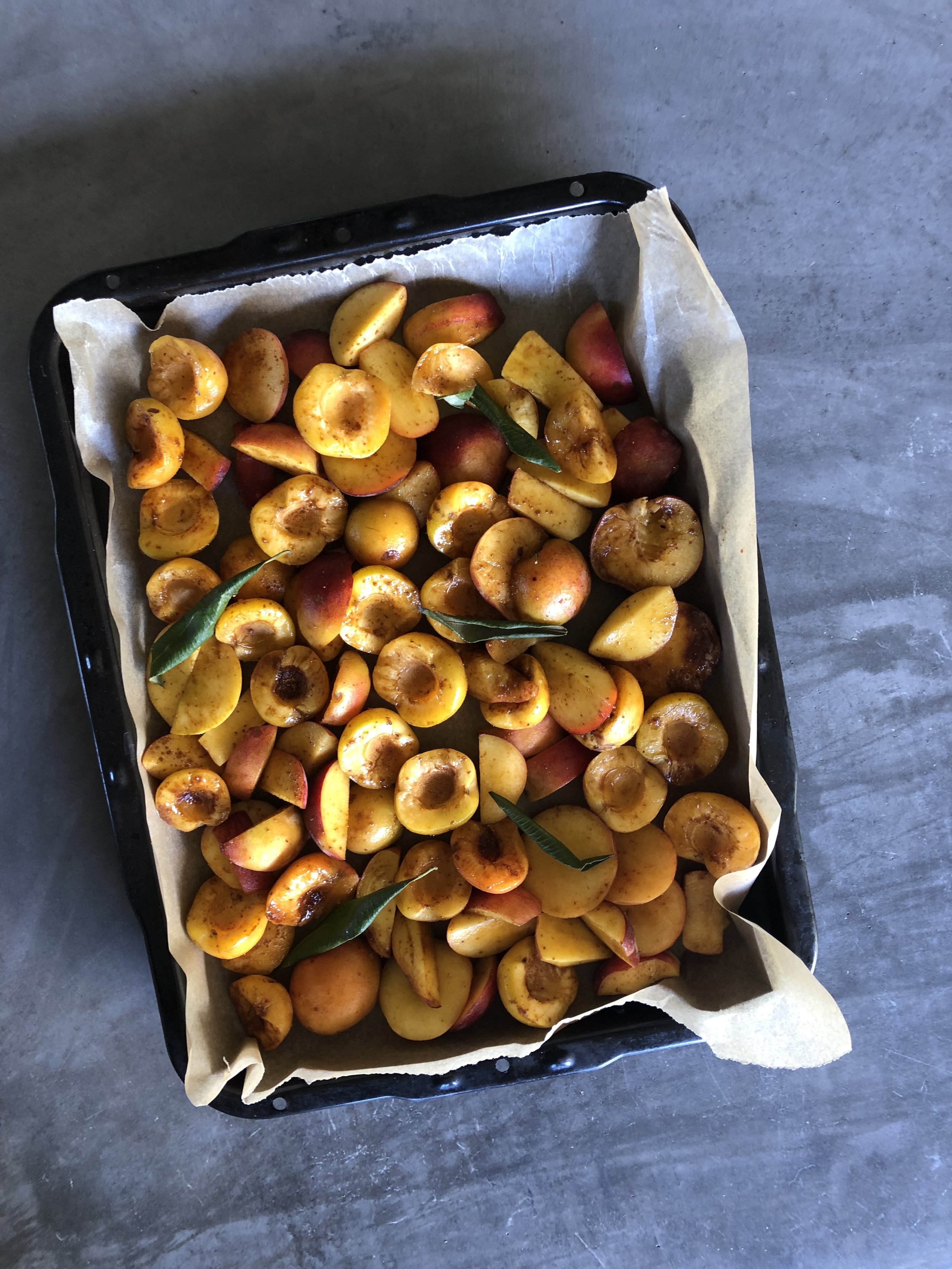 Baking tray with halved peaches on parchment paper