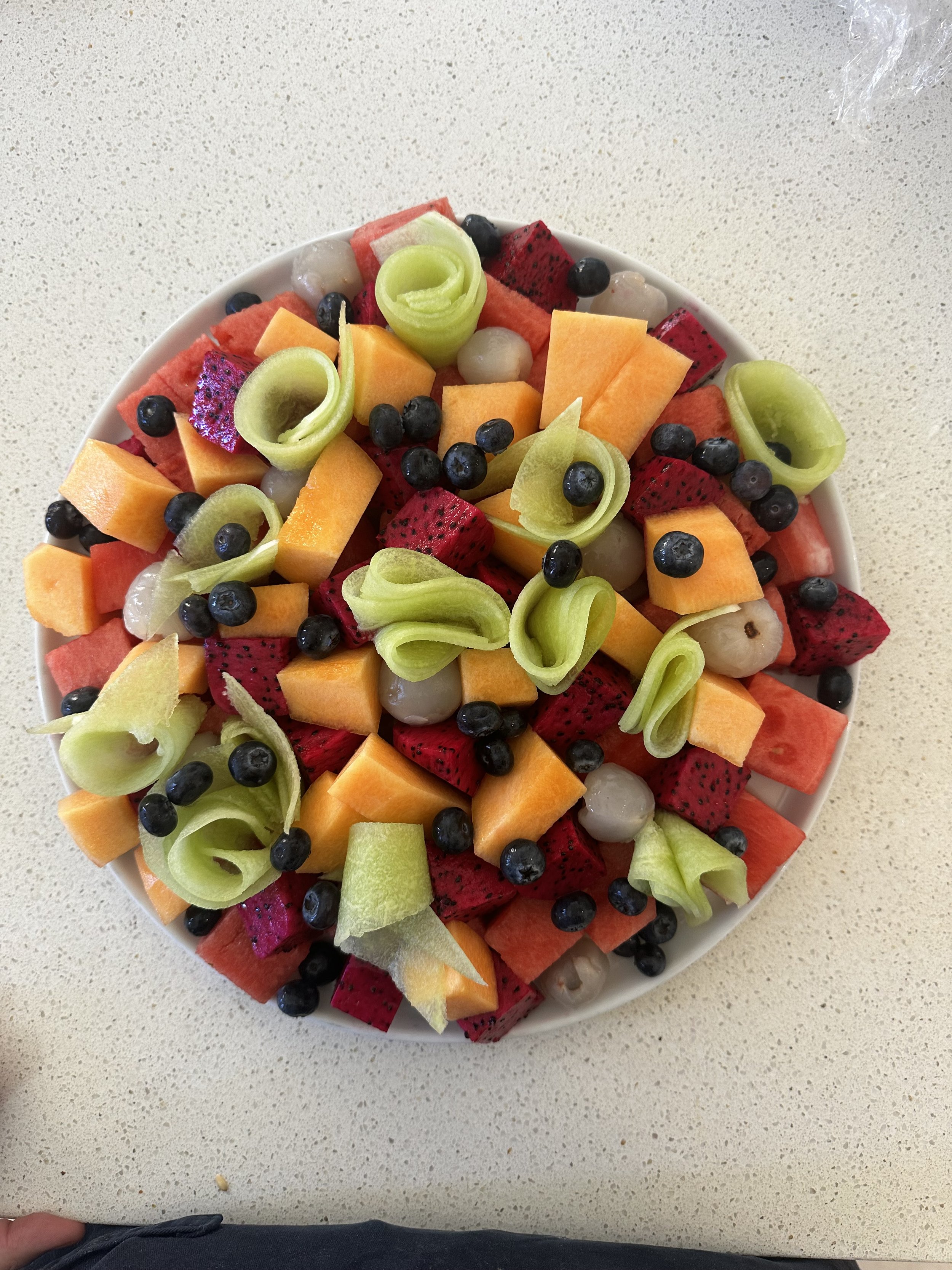 Plate of colorful fruit with kiwi, cantaloupe, dragon fruit, watermelon, blueberries, and lychee.