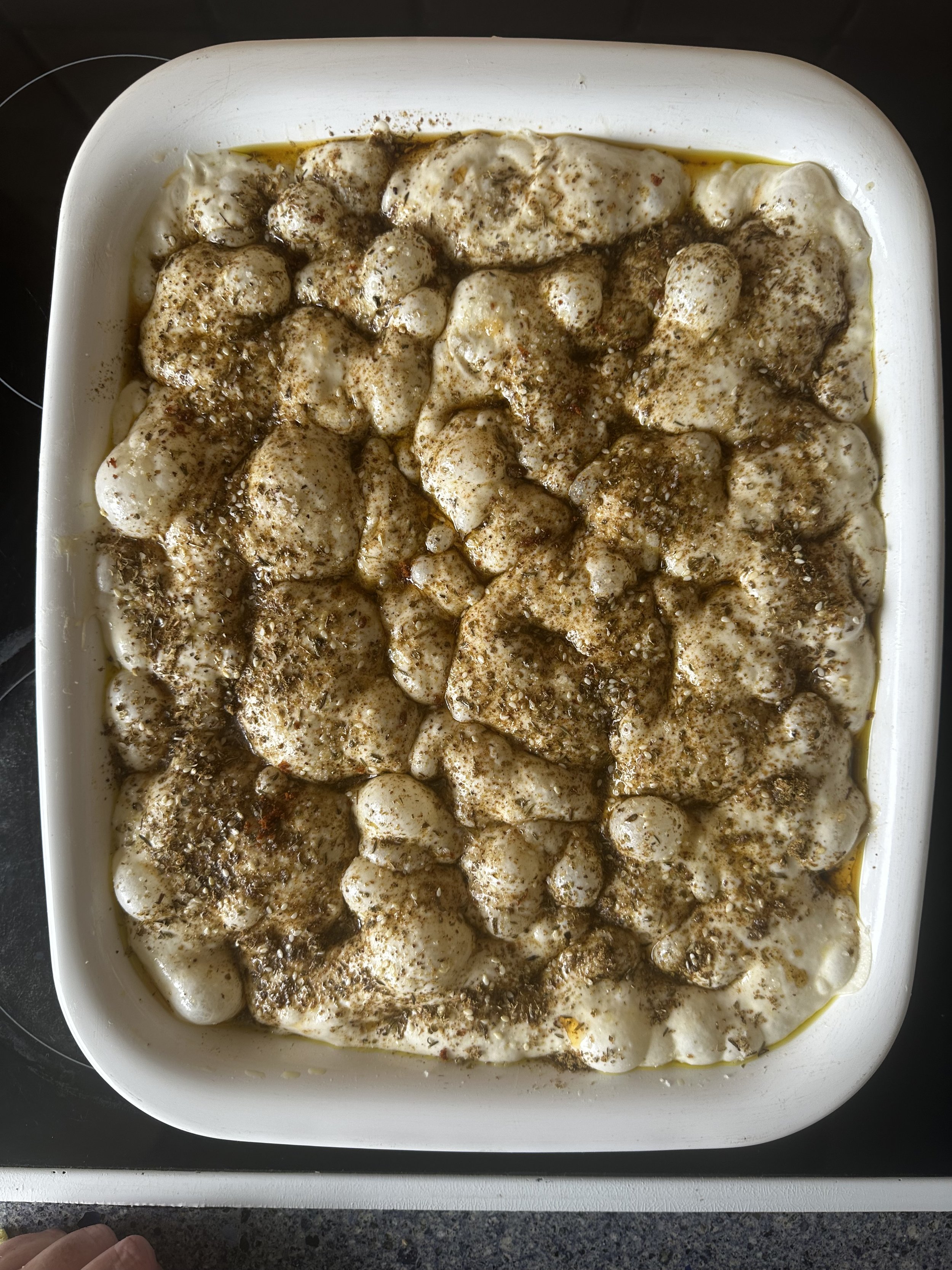 Baking dish with uncooked dough topped with herbs and spices.