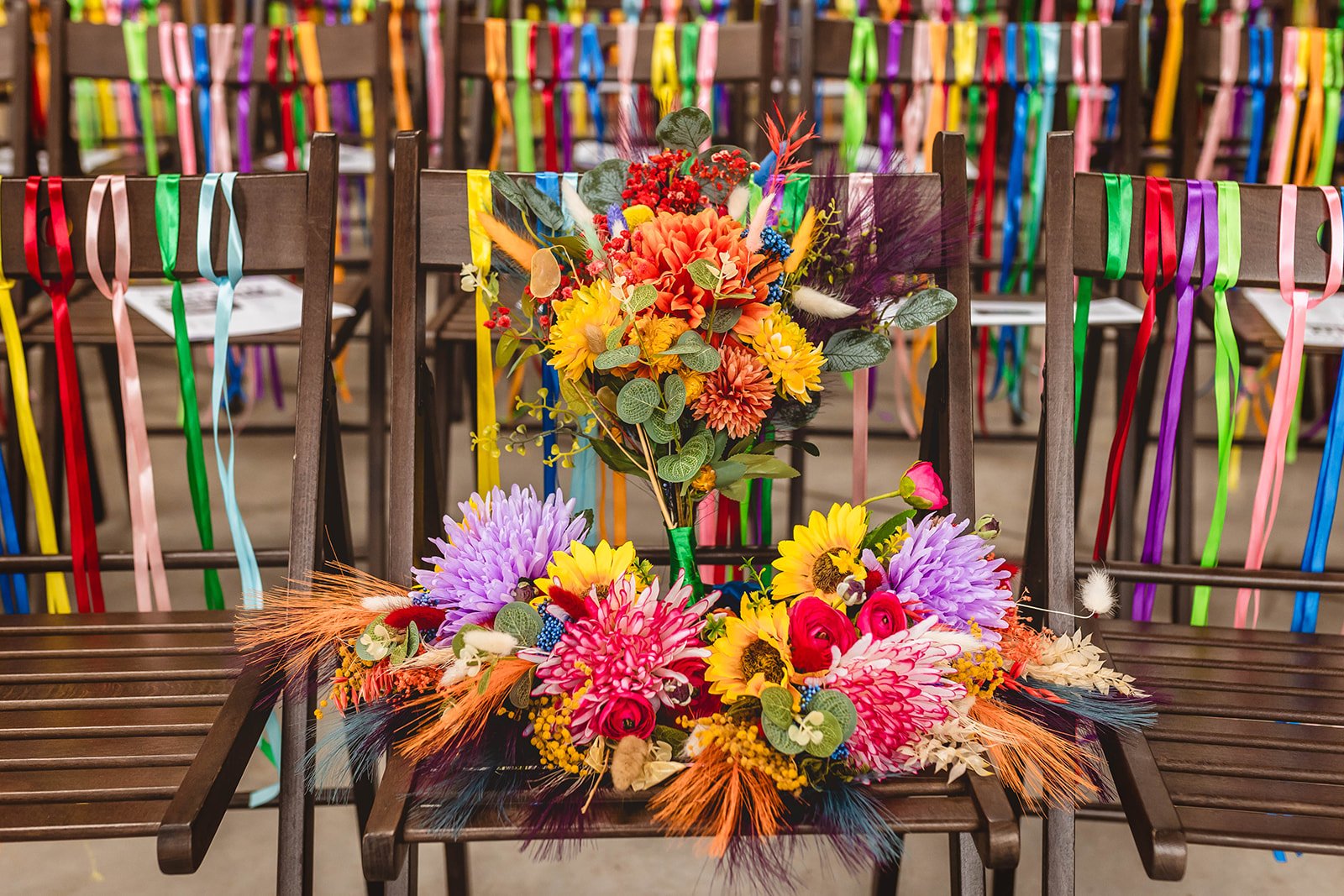 multicoloured bridal bouquets arranged on a wooden chair with rainbow ribbon decoration