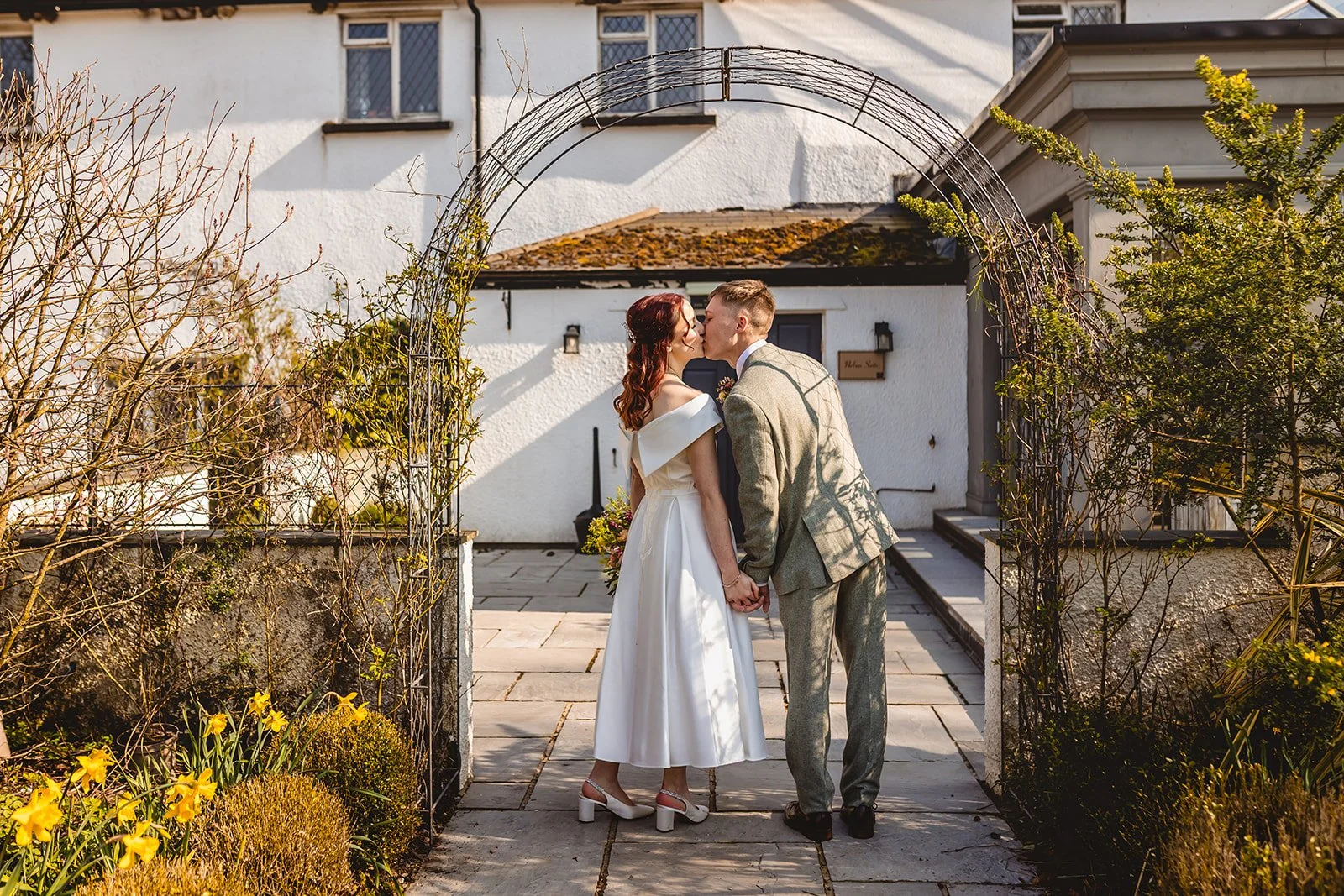 bride and groom kiss beneath an ivy arch outside llechwen hall on a bright and sunny spring wedding day
