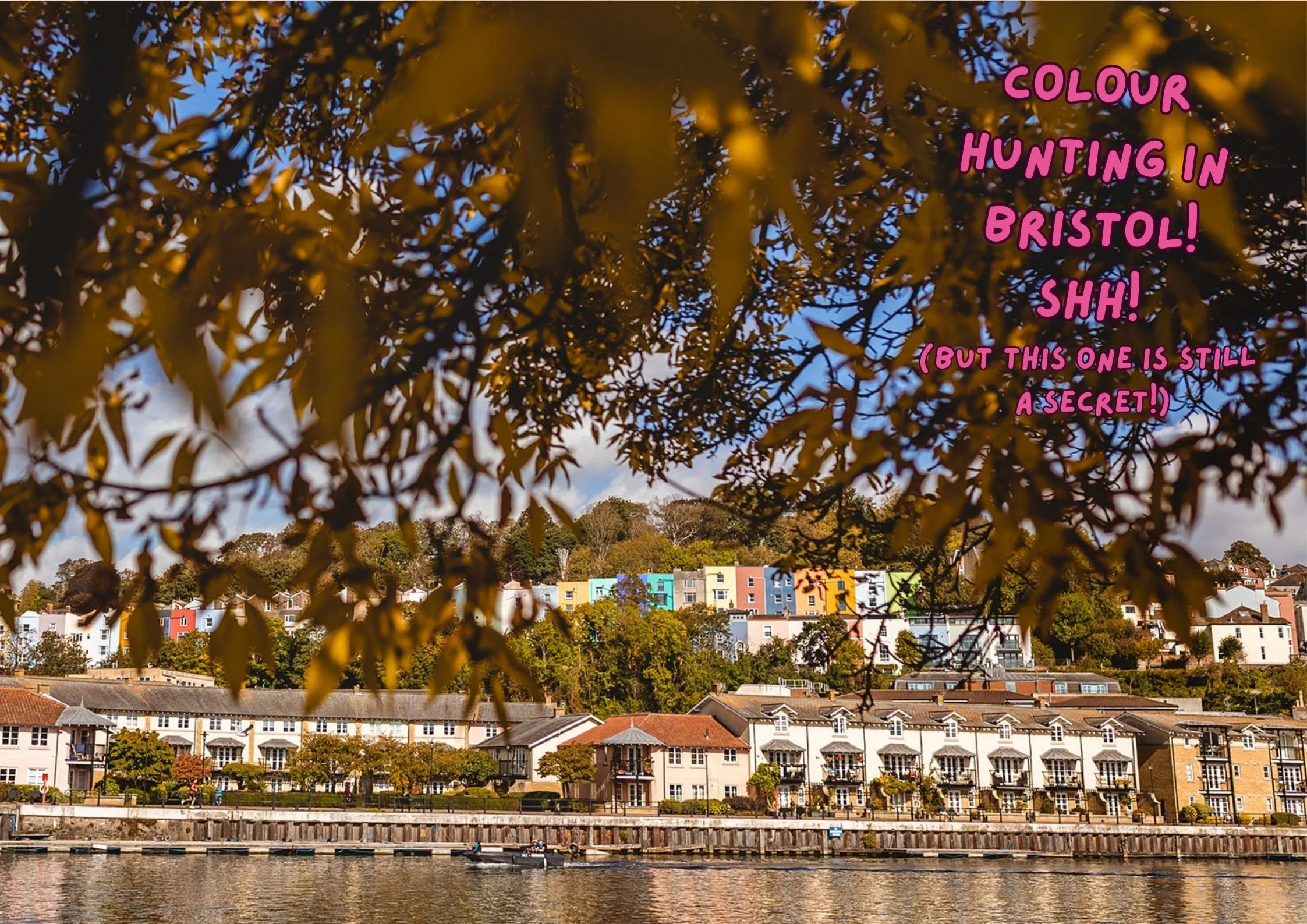 A LANDSCAPE PHOTOGRAPH THROUGH THE AUTUMN LEAVES OVERLOOKING THE DOCKS AND FAMOUS COLOURFUL HOUSES OF BRISTOL