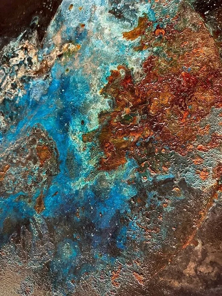 Close-up of a textured metal surface with patches of blue and reddish-brown patina.