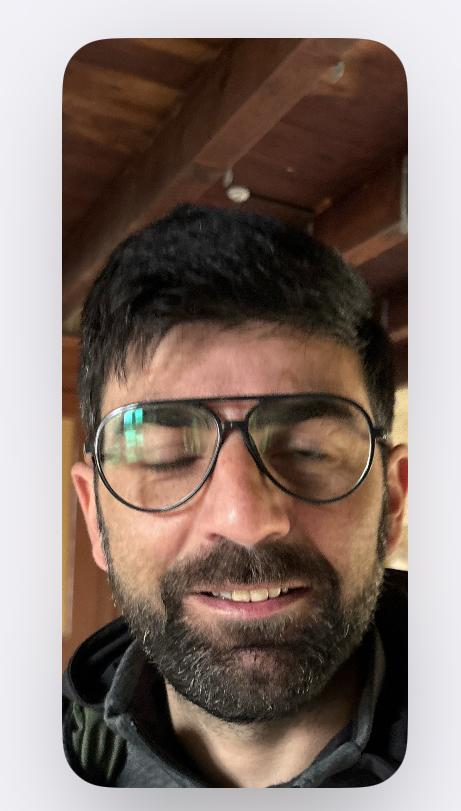 Un homme avec des lunettes, une barbe, souriant légèrement, en intérieur sous un plafond en bois.