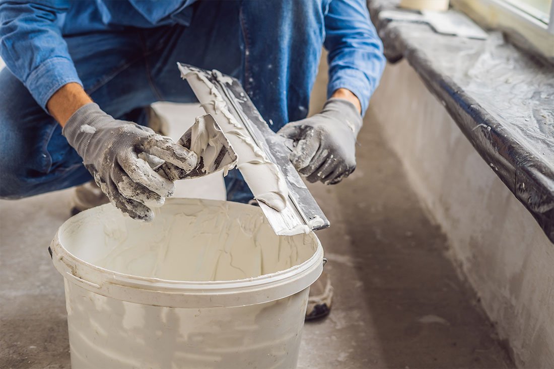 Personnes appliquant du plâtre sur un mur avec une spatule, dans une pièce en cours de rénovation.
