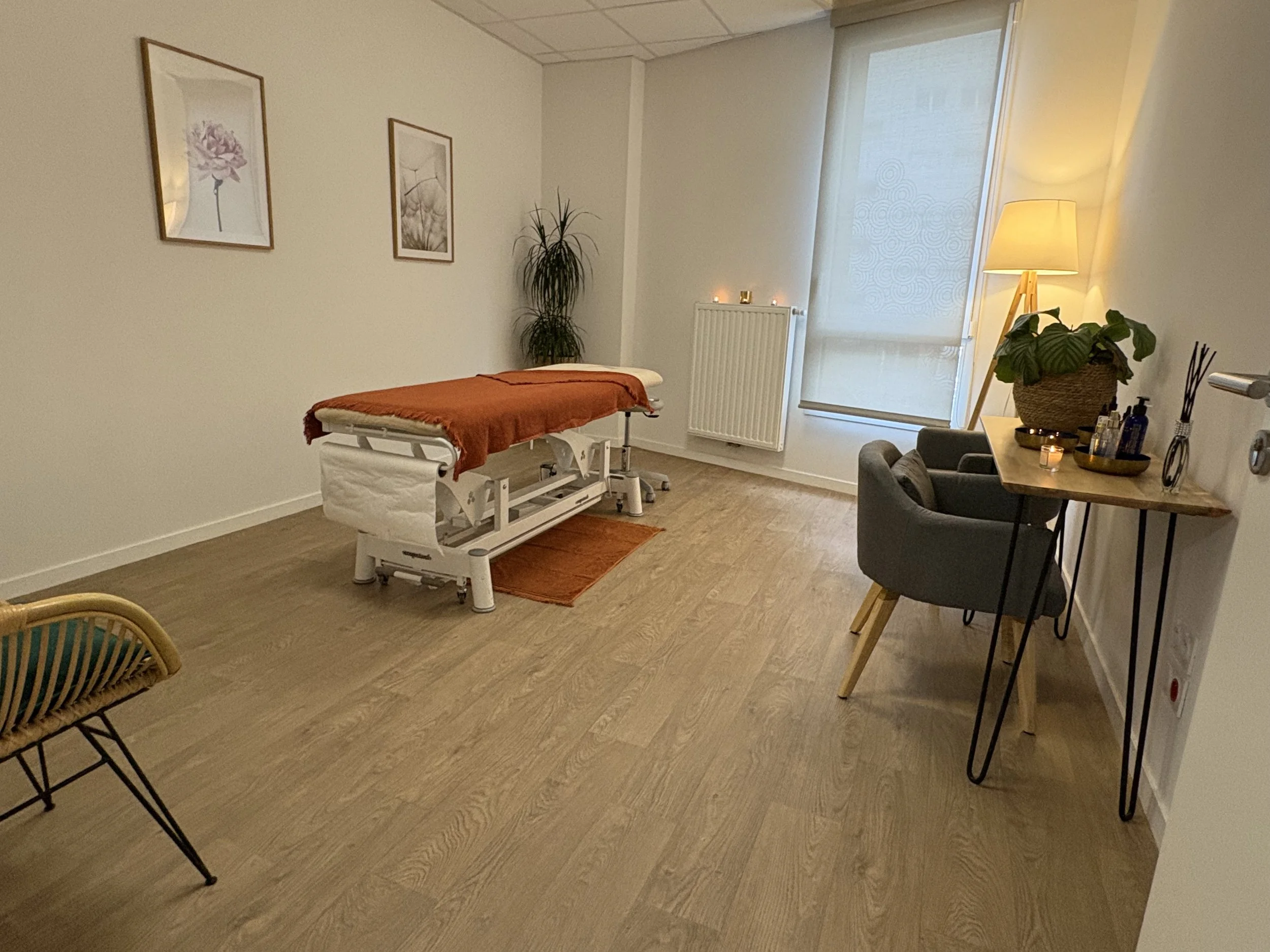 Salle de soin avec un lit de massage, une lampe, un bureau avec des plantes et des décorations
