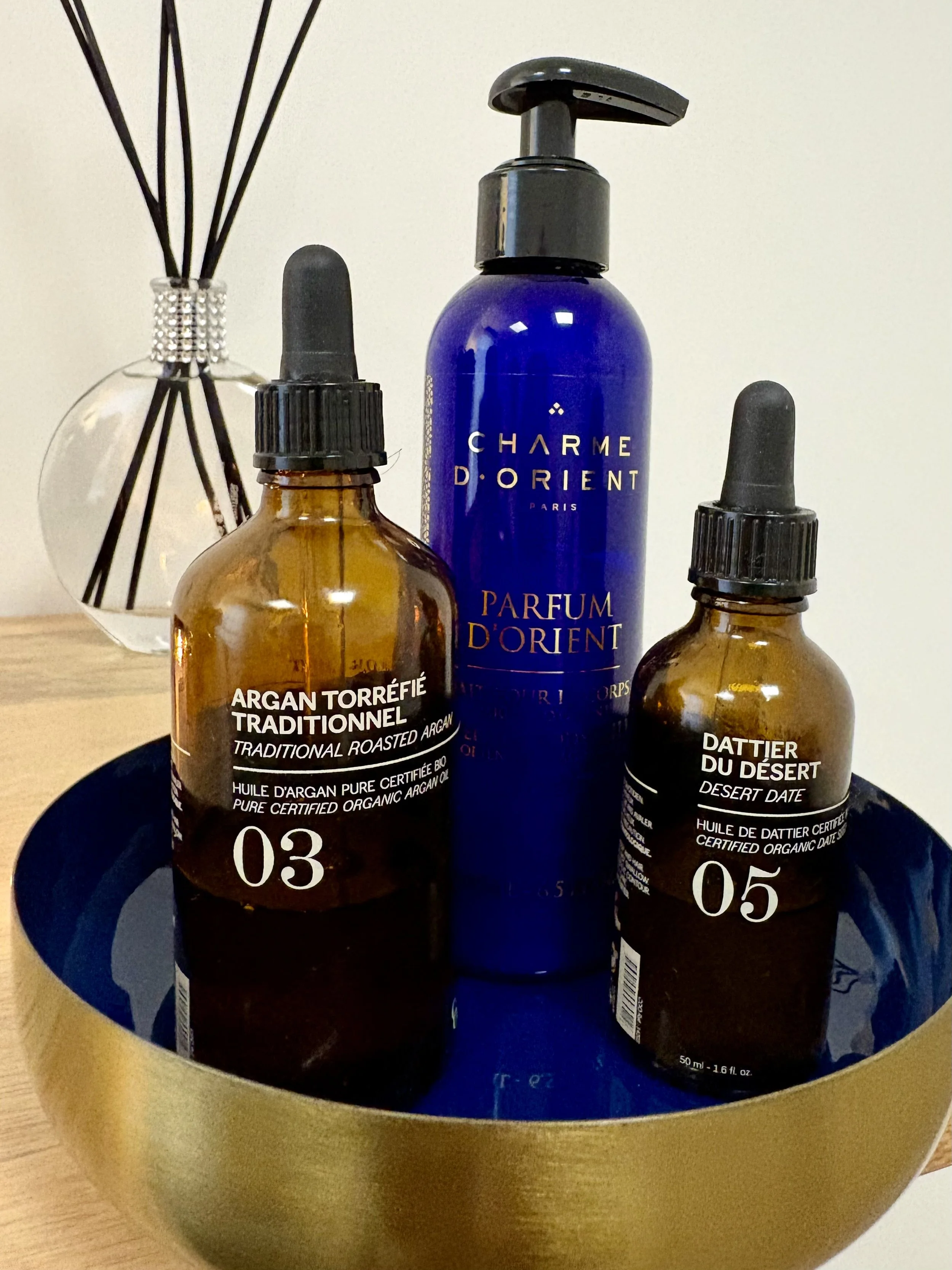 Trois flacons de produits de soins ou de beauté dans un récipient doré, avec un décor en verre en arrière-plan.
