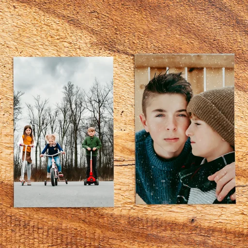 Two photos on a wooden surface. The left photo shows three children riding scooters and a girl with a bike outside on a cloudy day with leafless trees. The right photo shows two boys in close-up, one with a serious expression and the other looking at him, both in warm clothing.