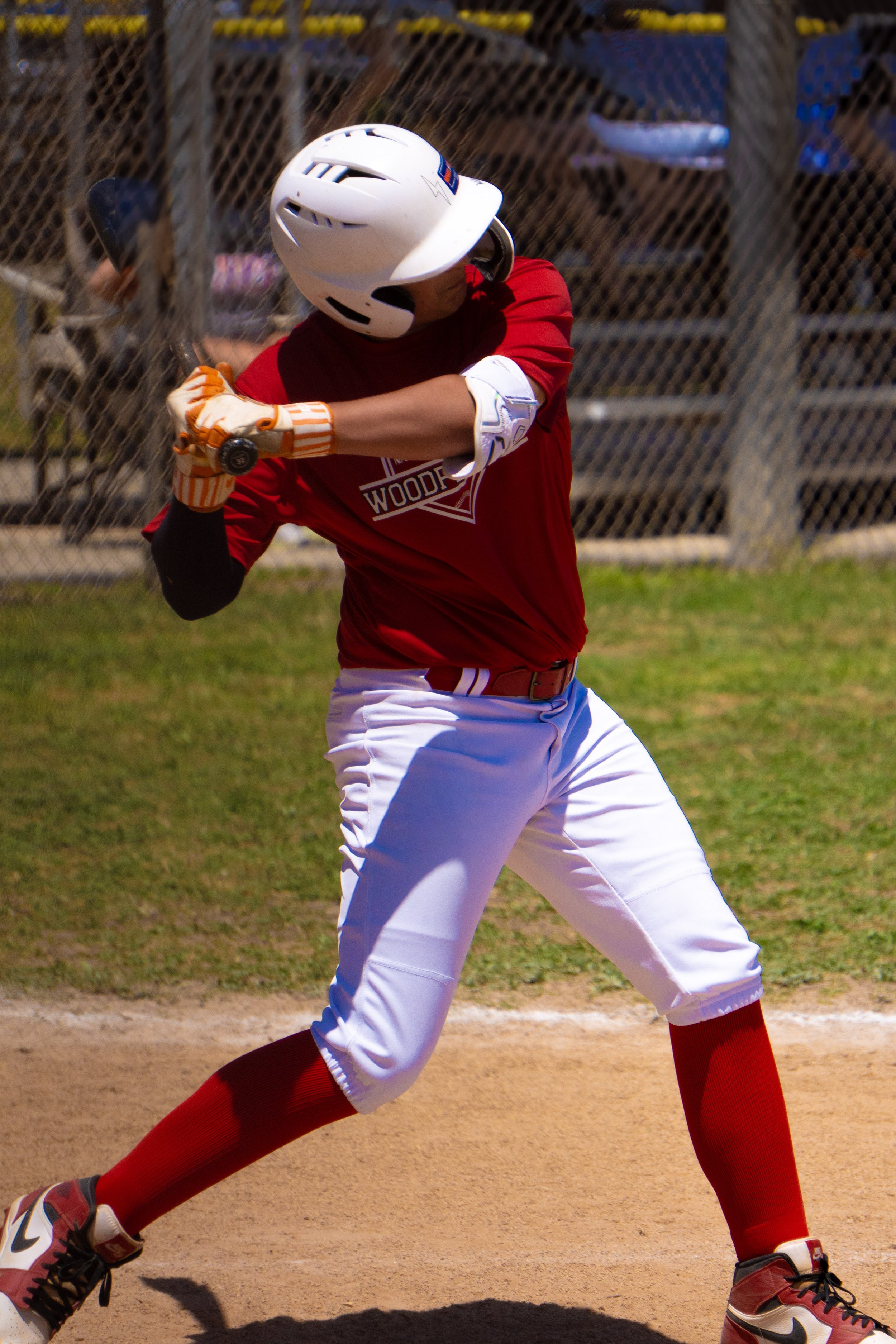 A baseball player in a red uniform with white pants, wearing a white helmet and orange gloves, swinging a bat on the field.