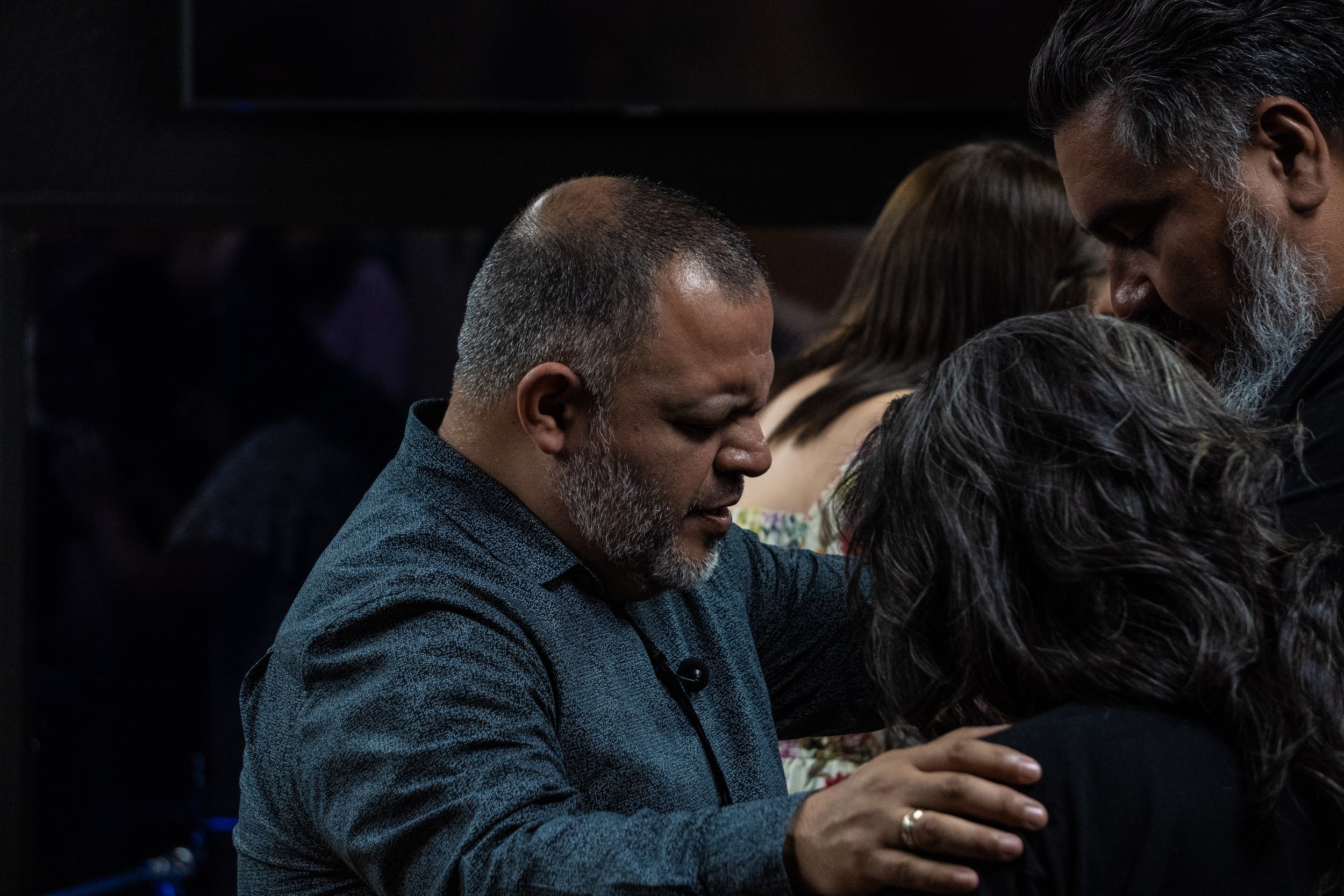 People praying with heads bowed and hands resting on shoulders in a solemn moment.
