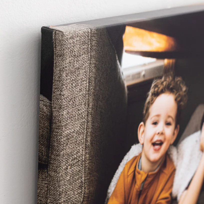 Close-up of a canvas print featuring a smiling young boy with curly hair, sitting on a couch in a cozy indoor setting.