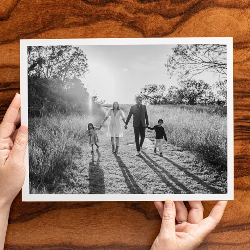 Black and white photo of a family holding hands and walking outdoors on a sunny day.