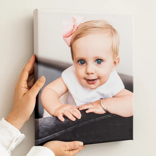 Close-up of a person holding a framed photo of a smiling baby girl with blue eyes and a pink bow in her hair.
