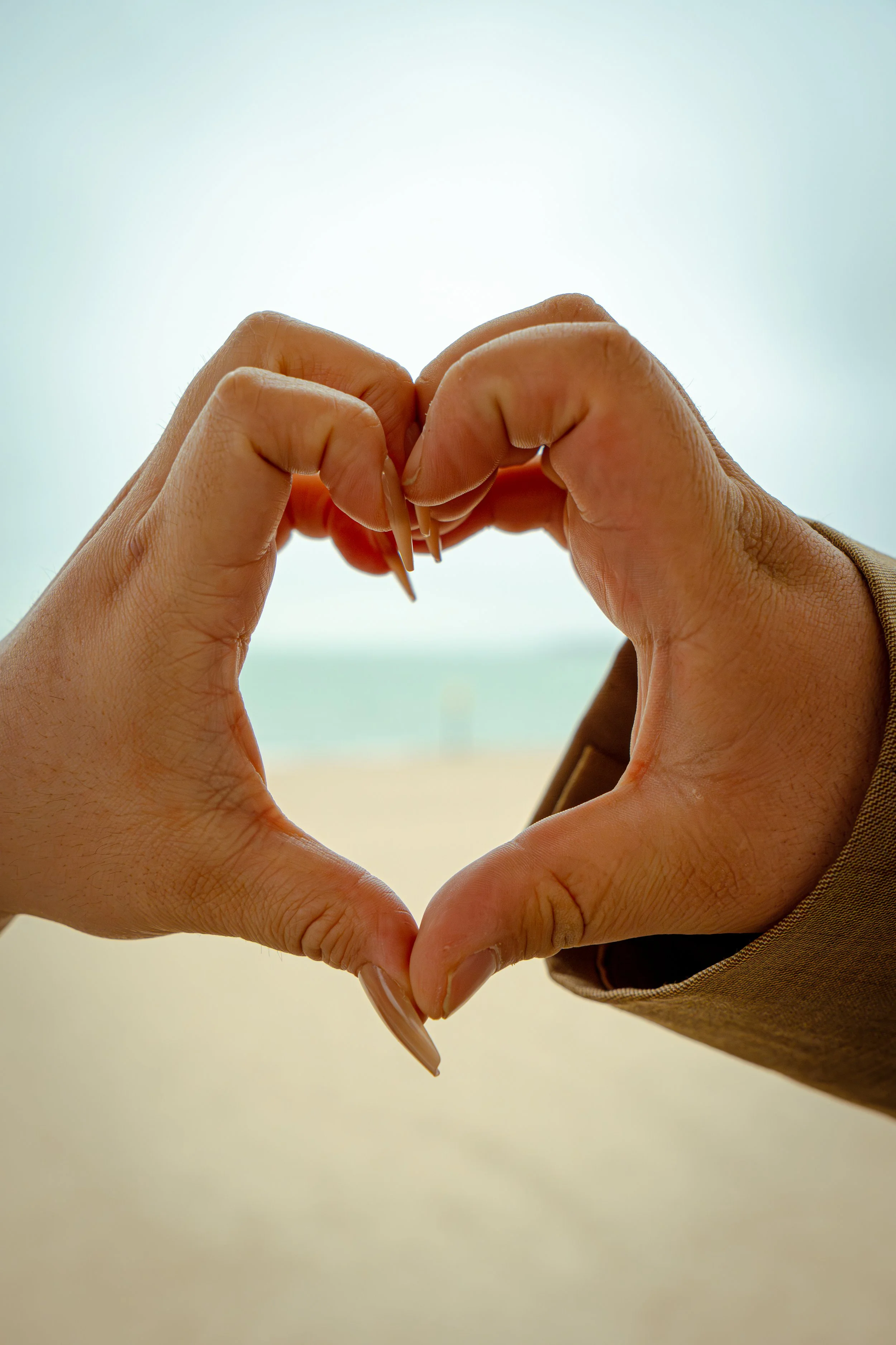Hands forming a heart shape with the sky and horizon in the background.