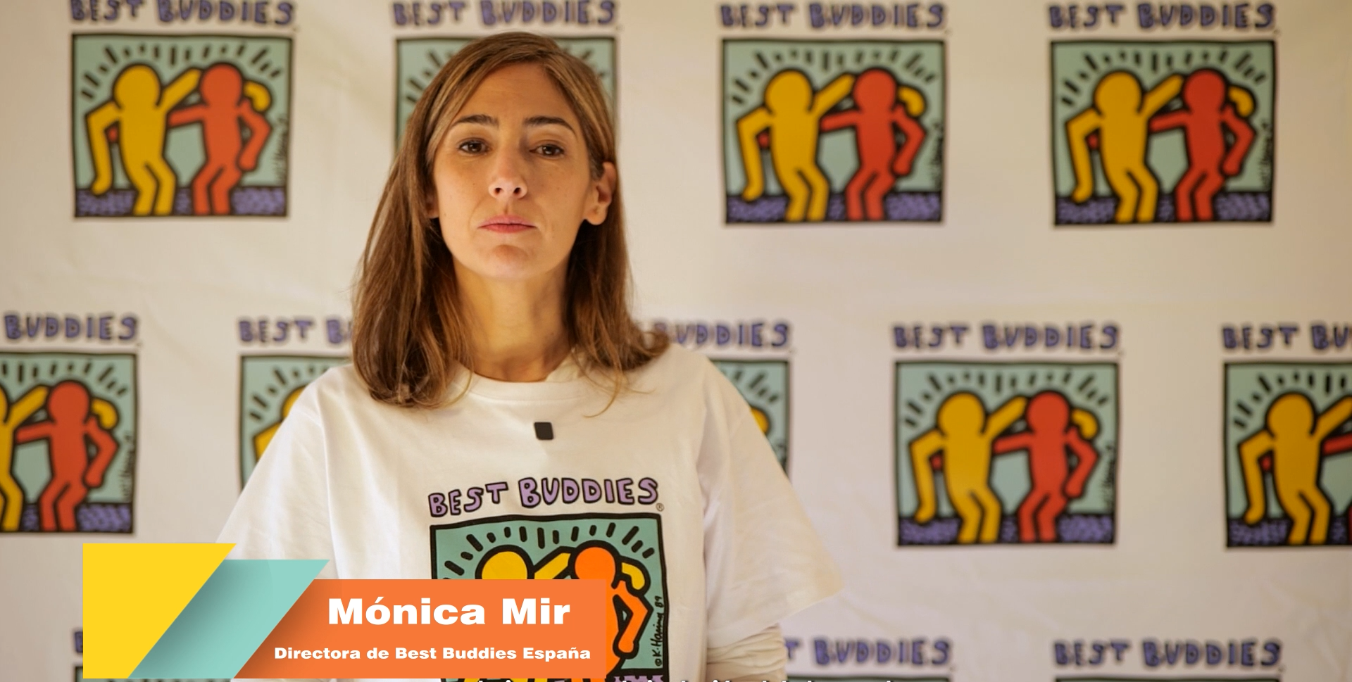 Mujer con camiseta blanca con el logotipo de Best Buddies, posando frente a un fondo decorado con varias copias del logo de Best Buddies.