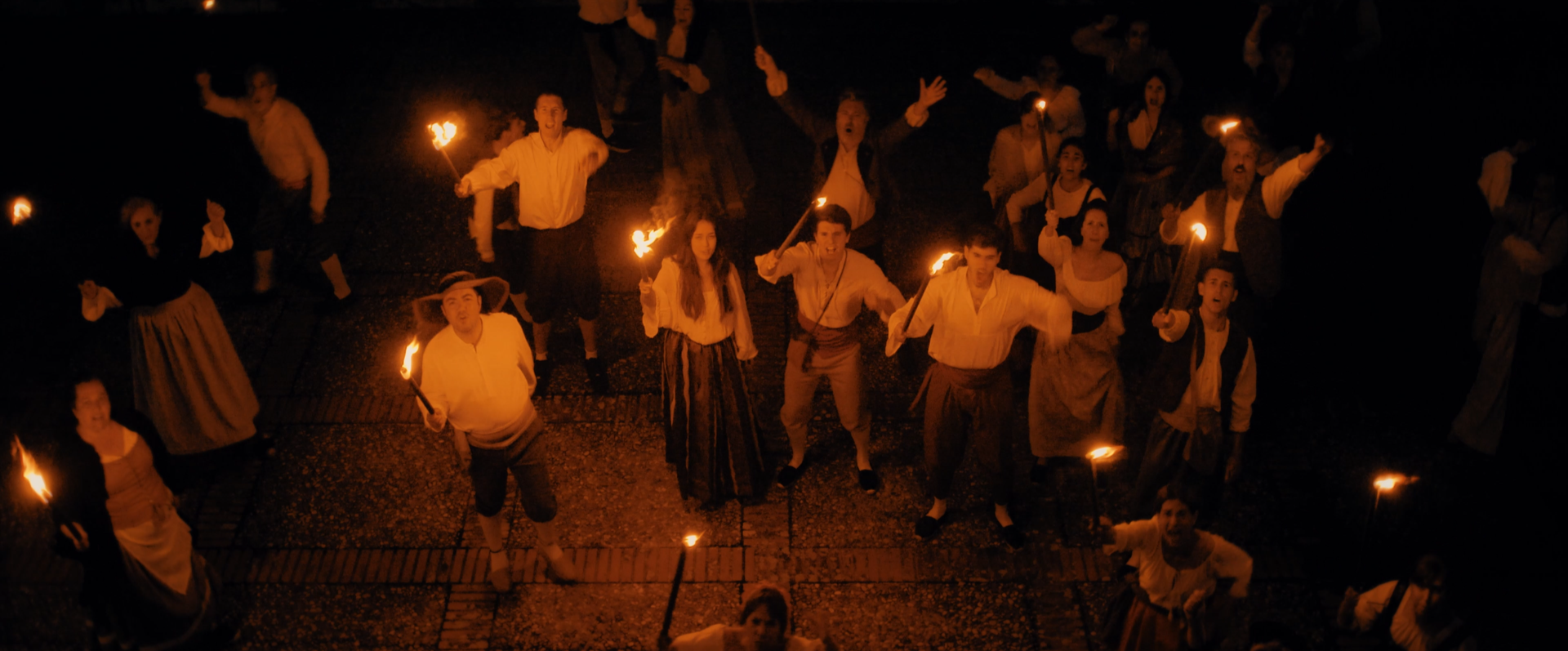 Grupo de personas en una celebración nocturna, sosteniendo antorchas encendidas, vestidas con ropa tradicional y moderna.