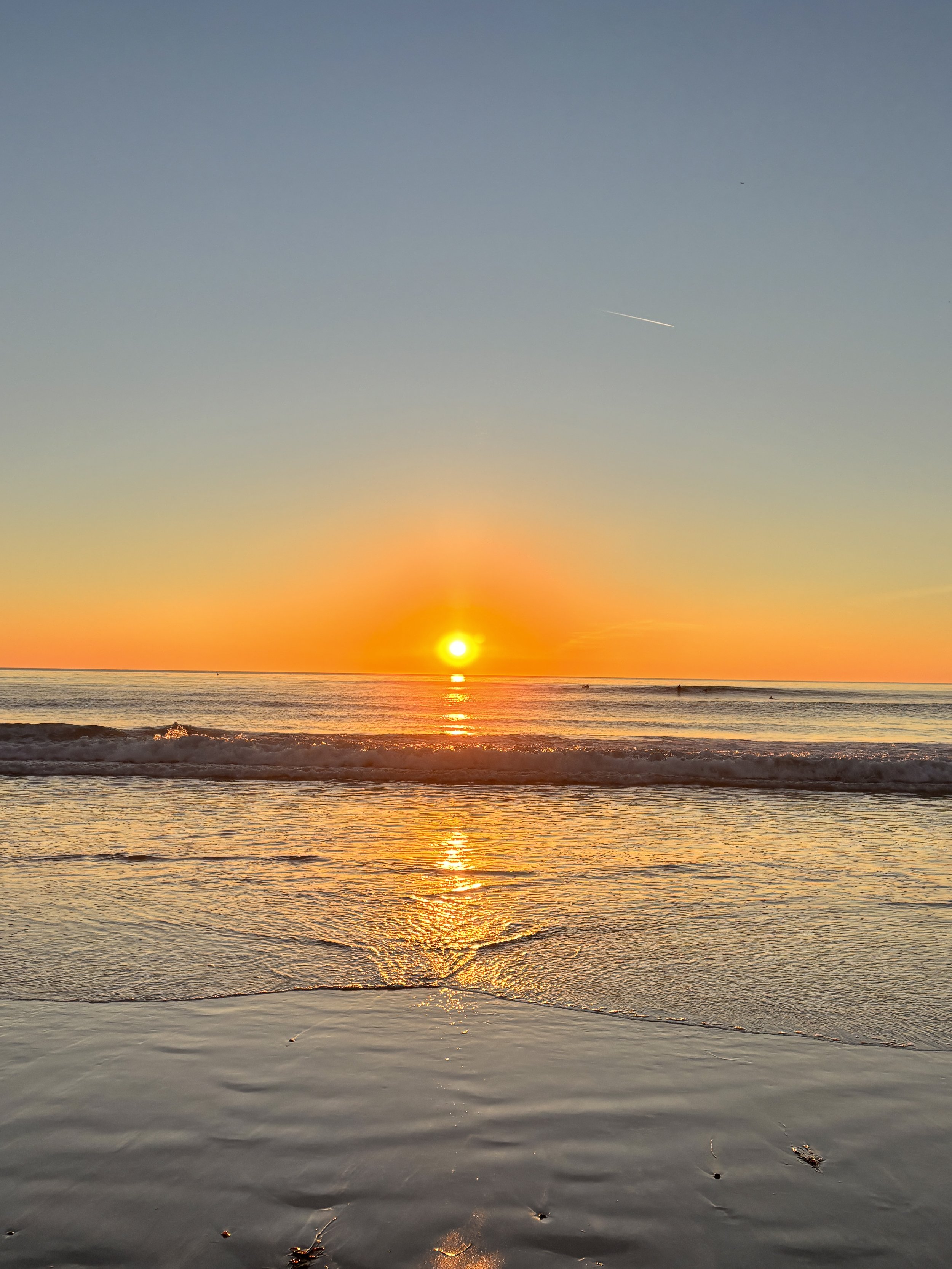 Sunset over the ocean with calm waves and a clear sky.