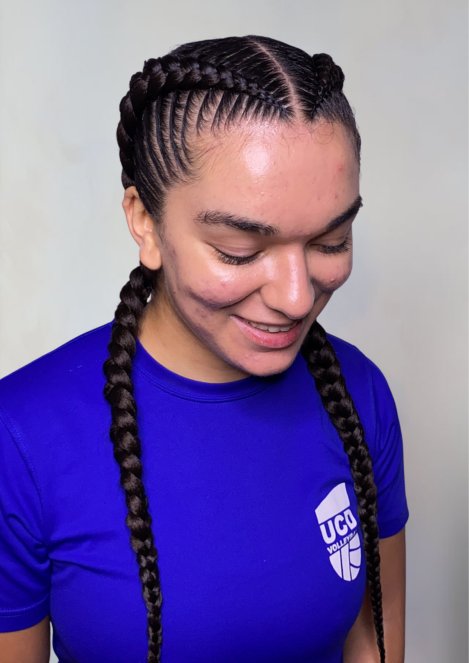 A young woman with braided hair wearing a blue UCS volleyball t-shirt, smiling and looking downward.