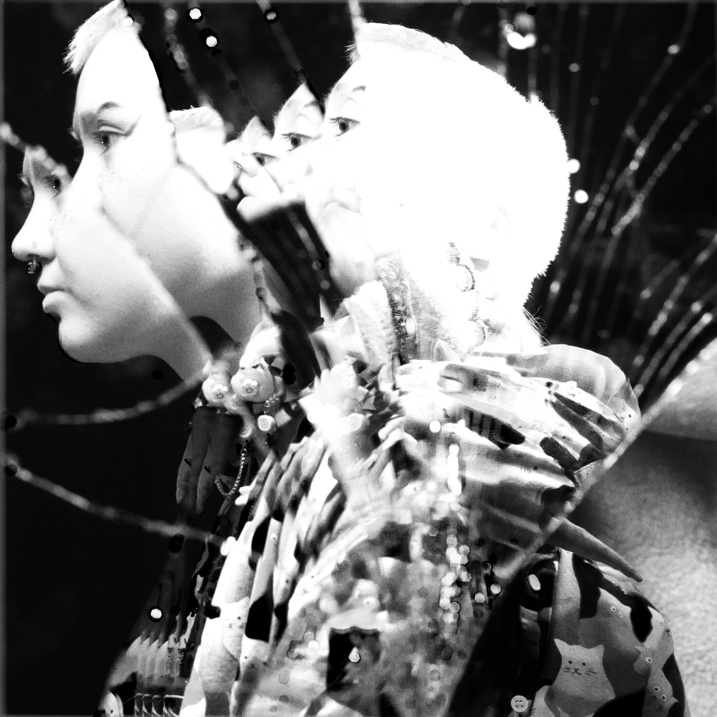 A black and white photo showing multiple layered images of a young person's face in profile and front, blending into each other with a reflective or artistic effect.