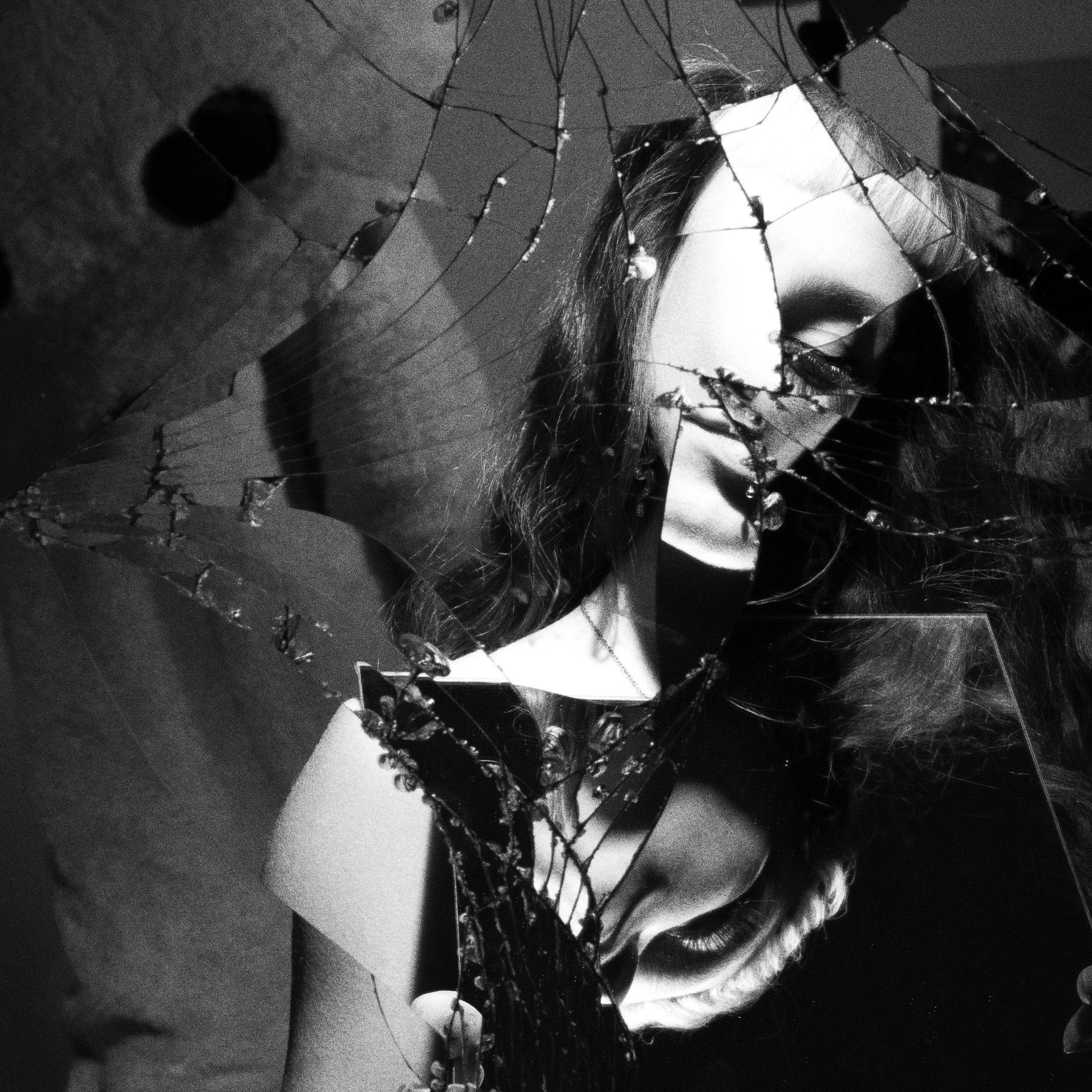 A shattered mirror reflecting a woman with long hair, wearing makeup and earrings, with cracks and broken glass fragments obscuring parts of her face.