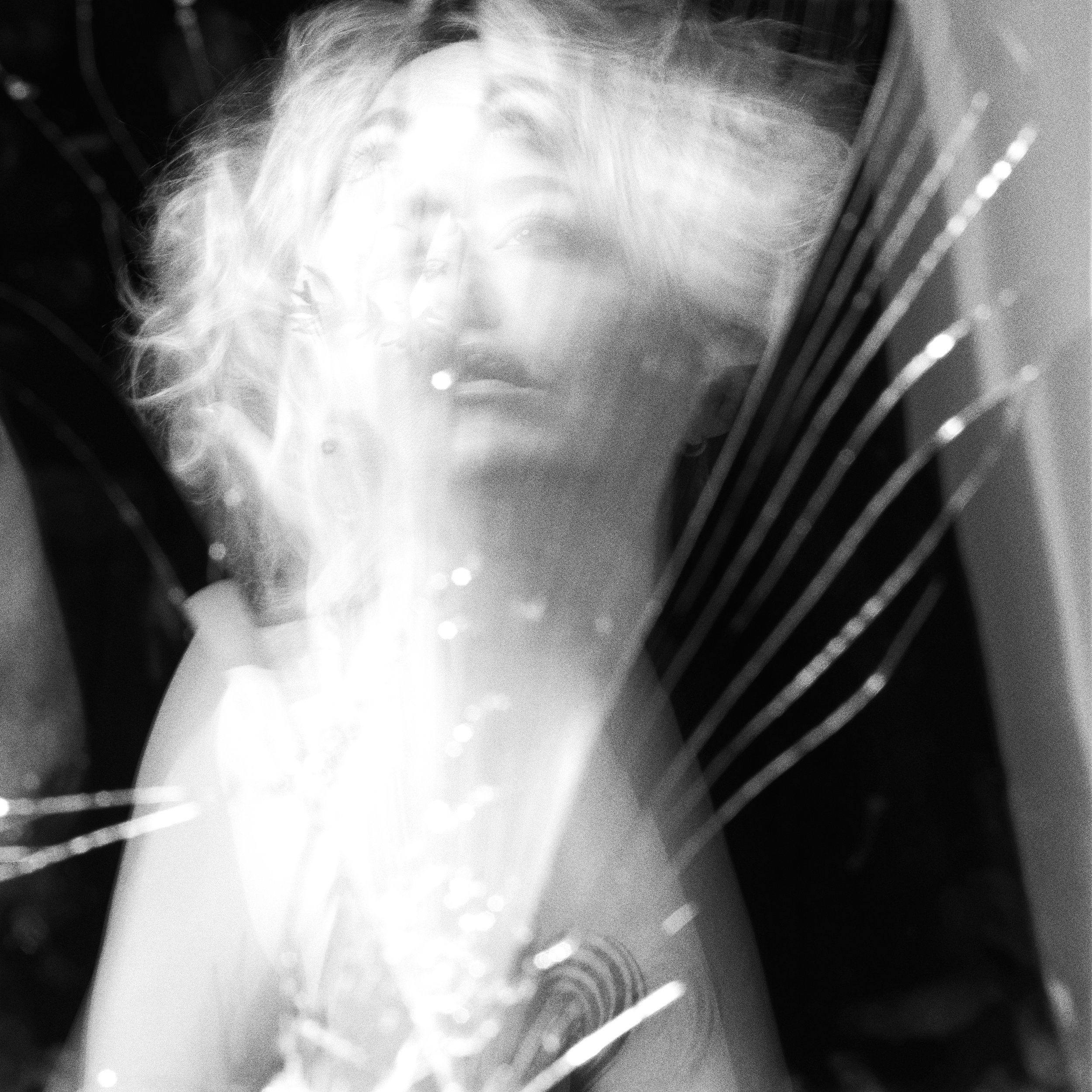 Black and white photo of a woman martini glass with a blurred reflection of her face behind it.