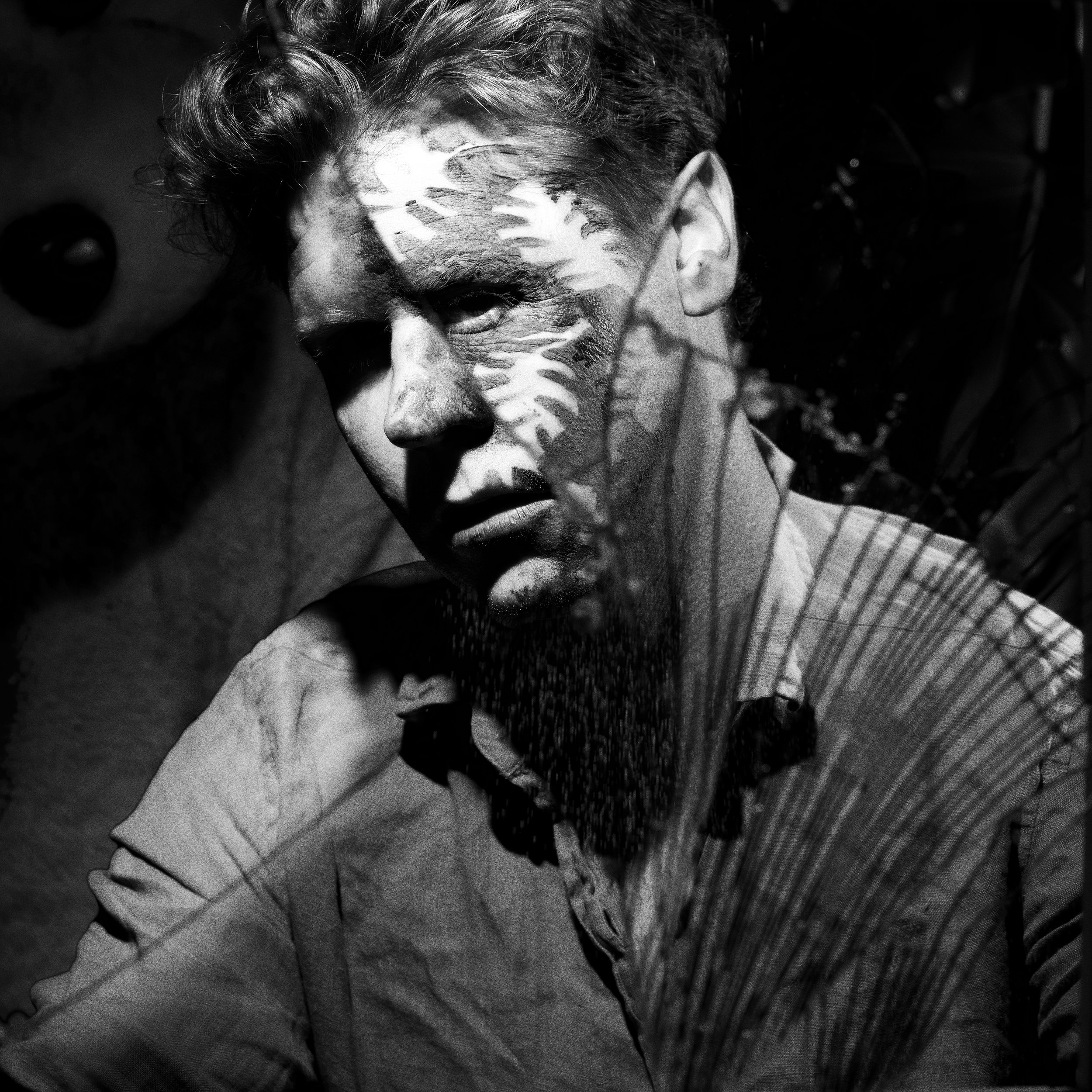 Black and white photo of a man's face, with a reflection or overlay of a butterfly on his face, creating a layered artistic effect.