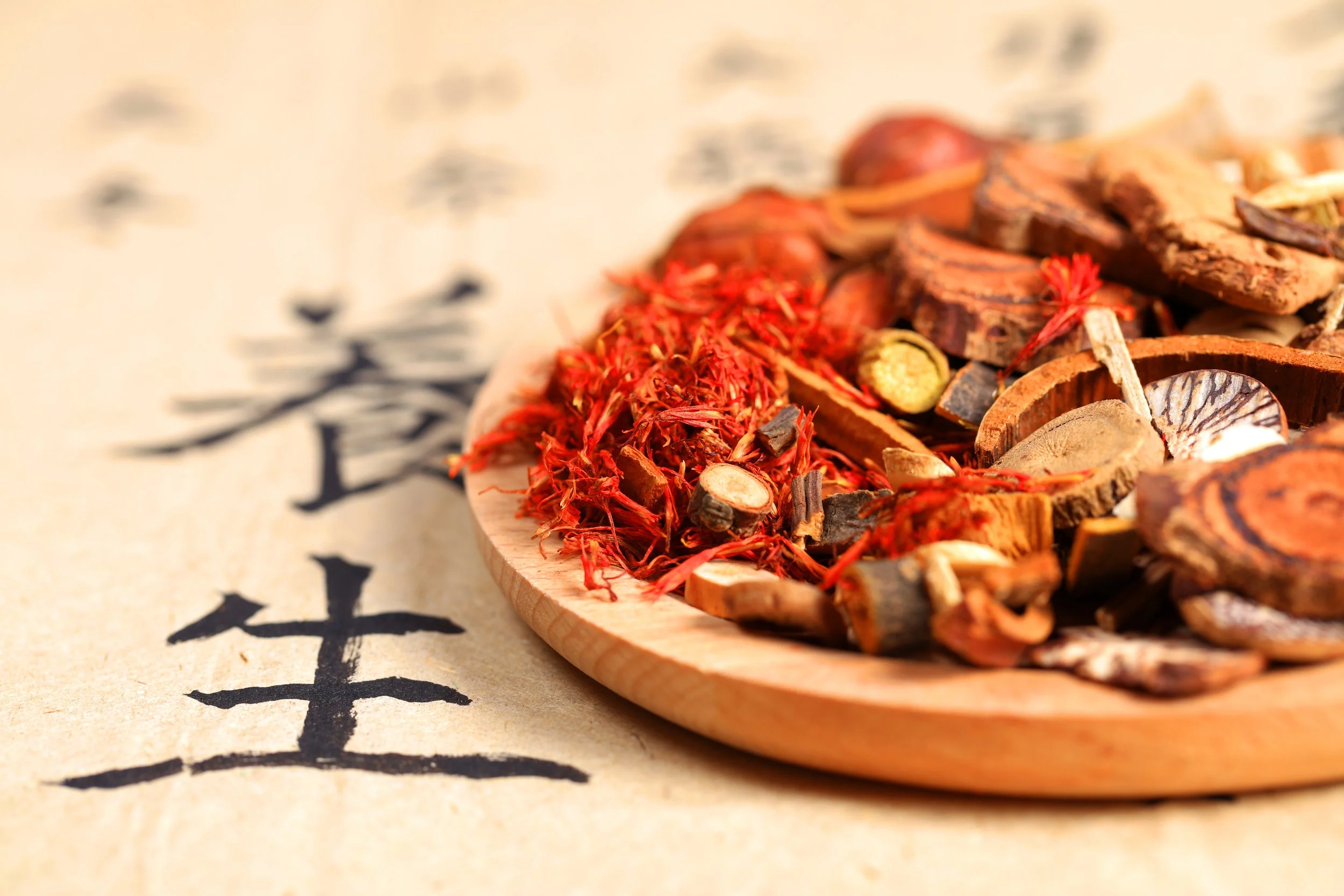 Close-up of traditional herbal medicine ingredients on a wooden plate placed on calligraphy paper with Chinese characters.
