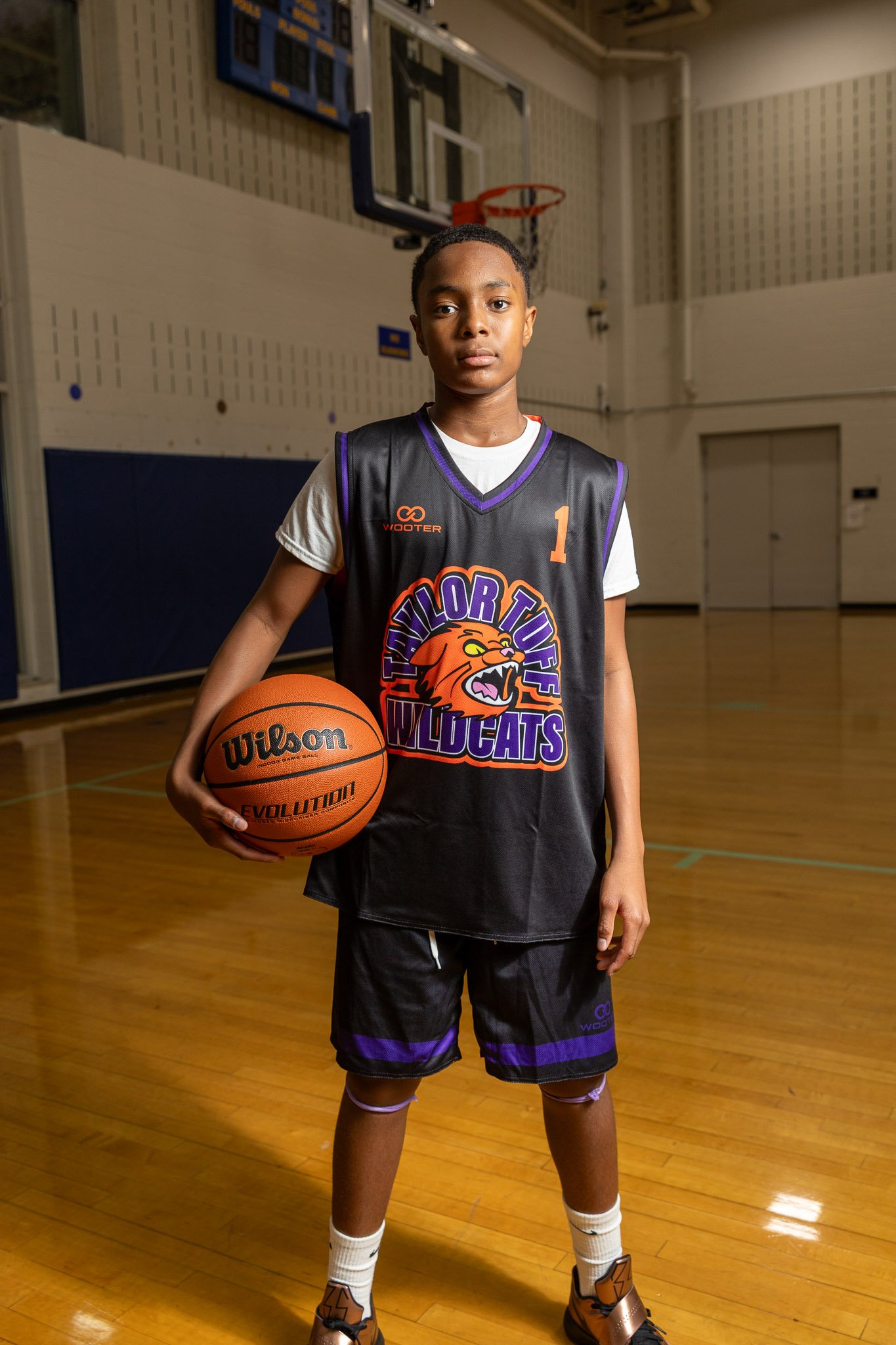 A young girl in a purple basketball jersey with the words 'Taylor Tuff Wildcats' and number 3, spinning a basketball on her finger inside a gymnasium.