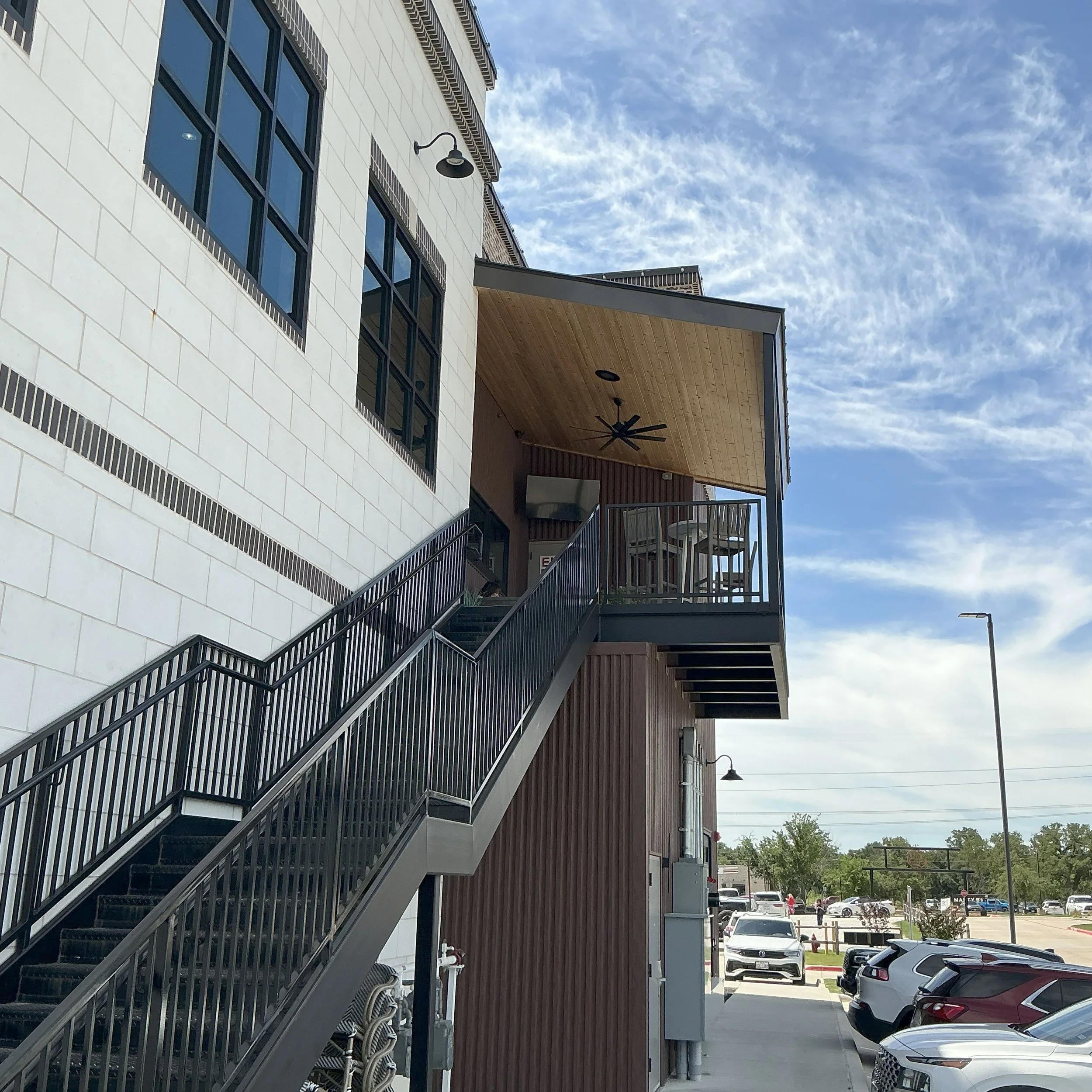 An apartment building with stairs leading up to a balcony with a ceiling fan, under a partly cloudy sky.