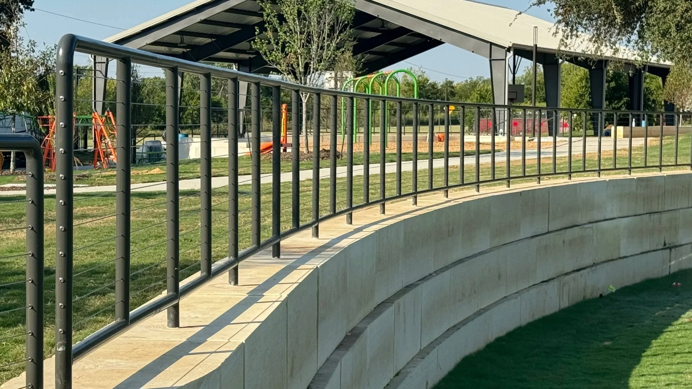 A park with a curved concrete wall and black metal handrail. 