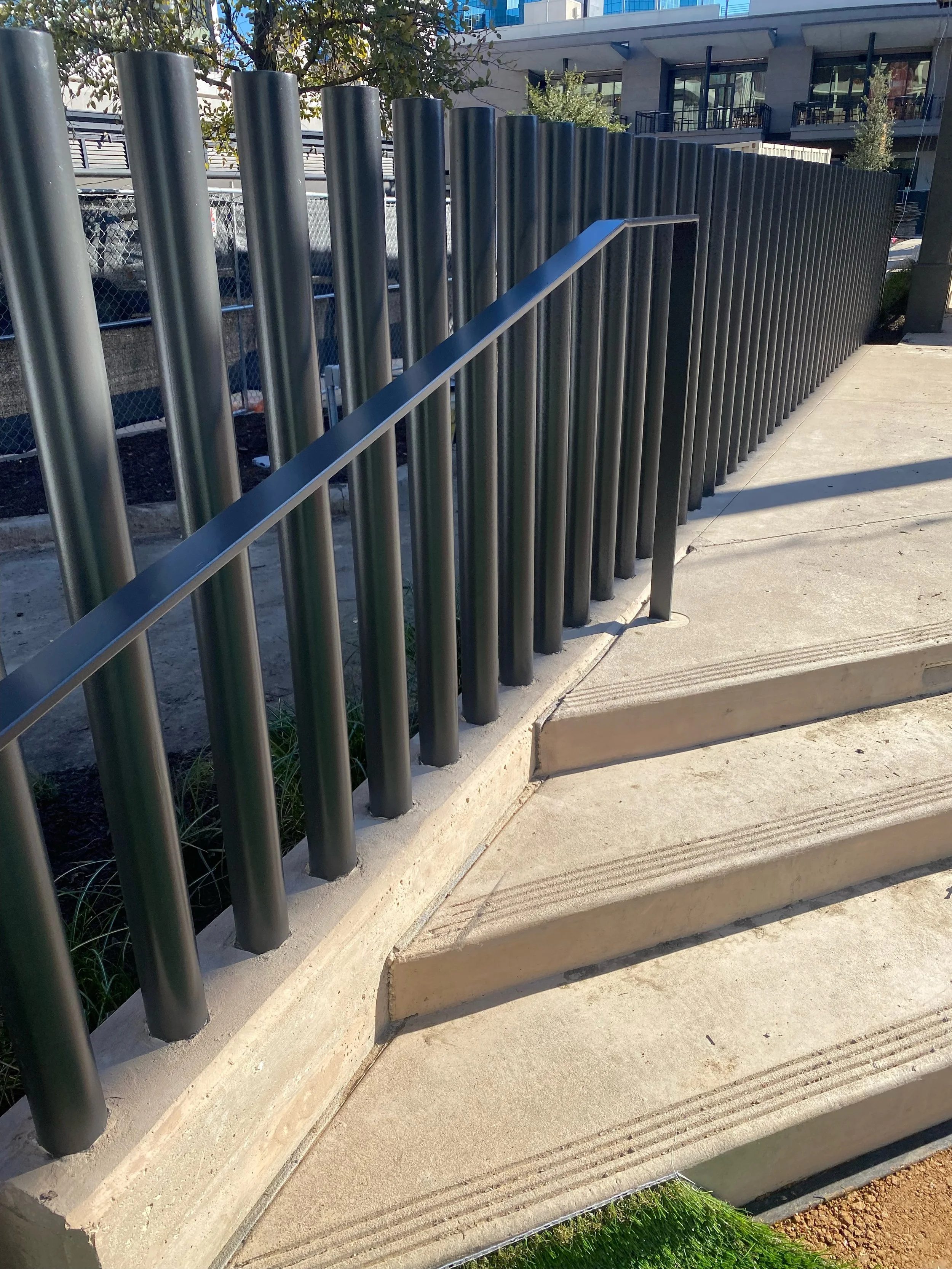Concrete stairs with a metal handrail, outside urban setting, with nearby buildings and trees.