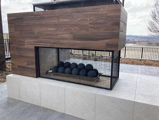 Modern outdoor fire pit with black spheres, surrounded by wooden panels and white tiled base.