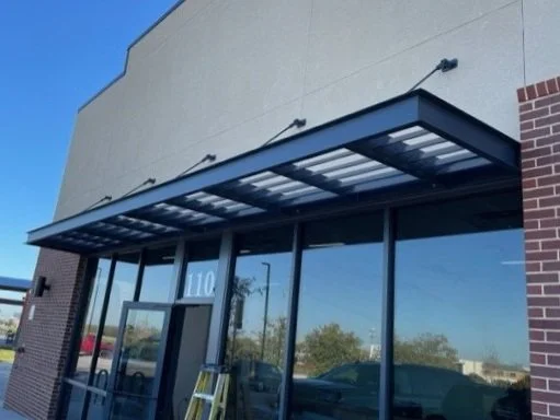 Front of a commercial building with large glass windows, a metal sunshade canopy