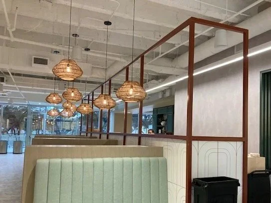 Interior view of a modern restaurant with hanging woven pendant lights, pastel green booths, and wooden dividers.