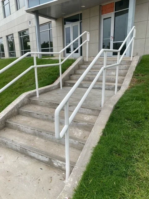 Concrete stairs with white handrails leading up to building entrance, with grassy area on each side.