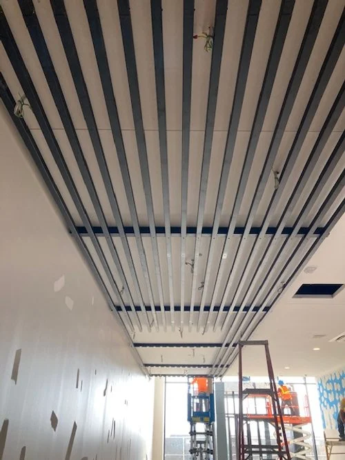 Ceiling with black metal slats, construction equipment, and scaffolding in a room under renovation.