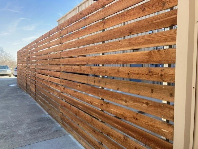 Wooden slat fence along a parking lot with cars, set against a clear sky.