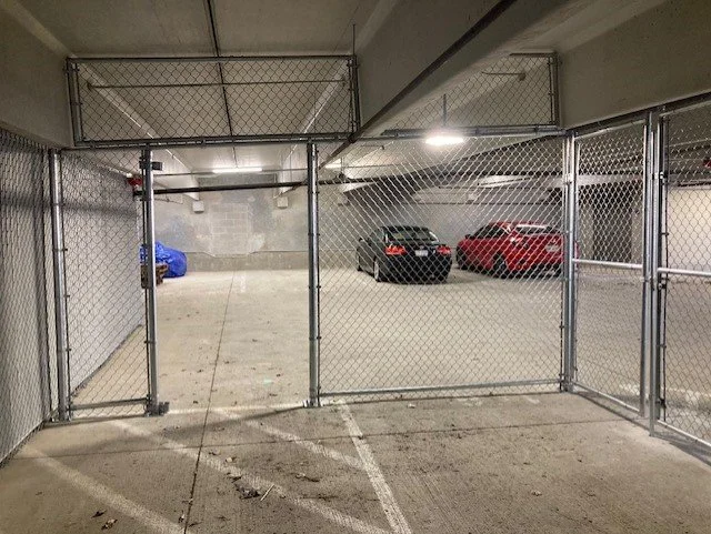 Fenced parking area with two cars, one black and one red, in an underground parking garage.