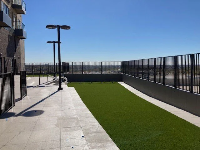 Rooftop terrace with artificial turf, metal railings, and modern outdoor lighting under a clear blue sky.