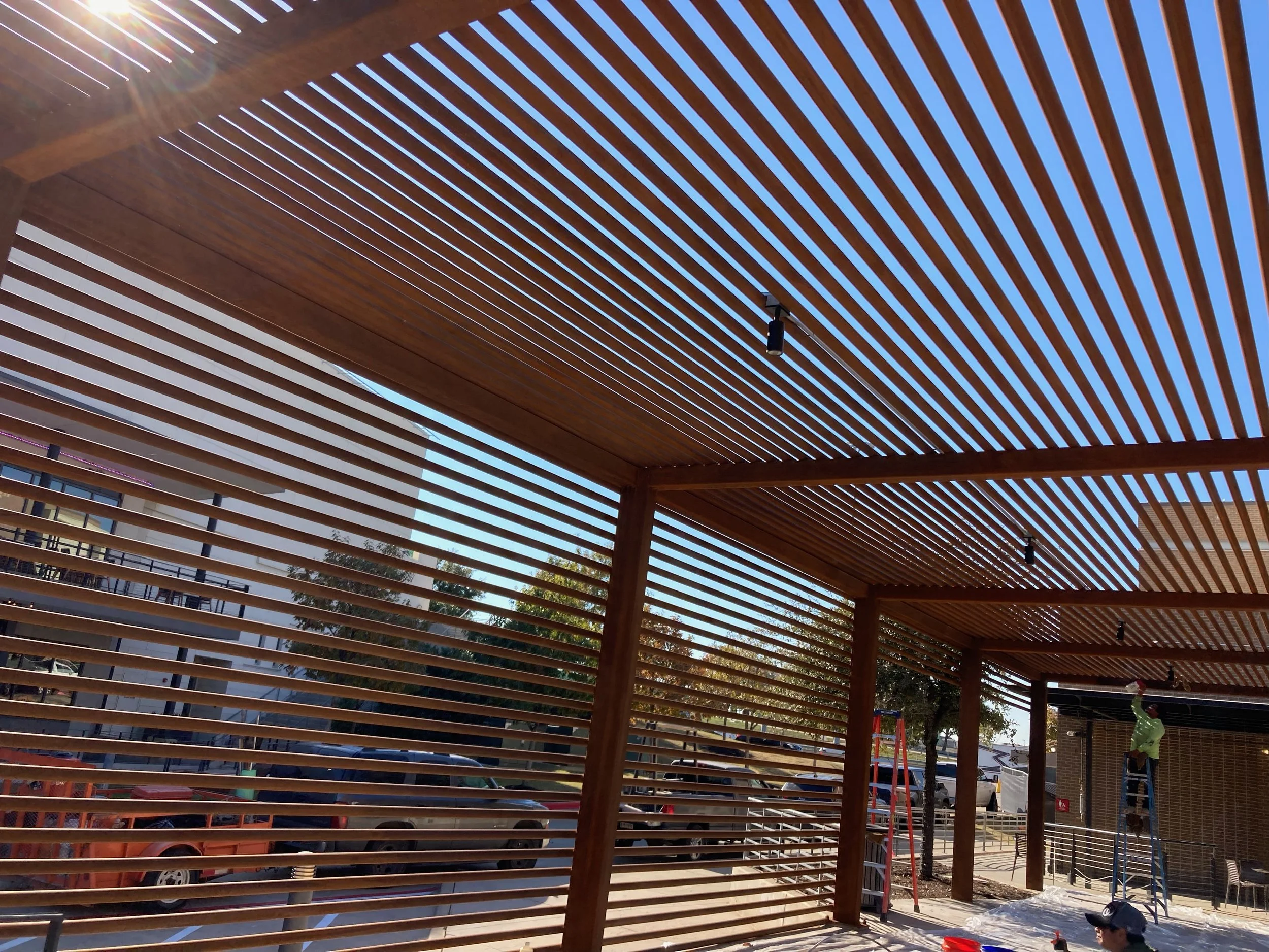 Construction site with wooden slat structures and workers installing a ceiling.