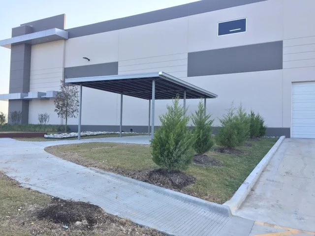 Exterior of a modern building with a parking area and small trees in landscaped beds.