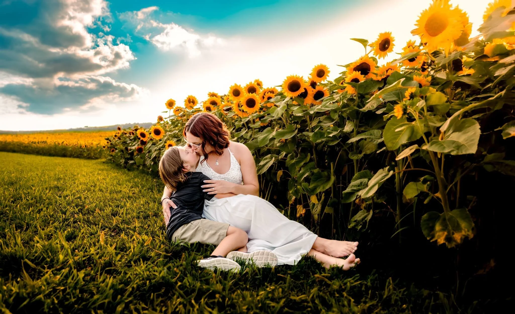 A woman and a young boy sharing a kiss in a sunflower field during sunset.