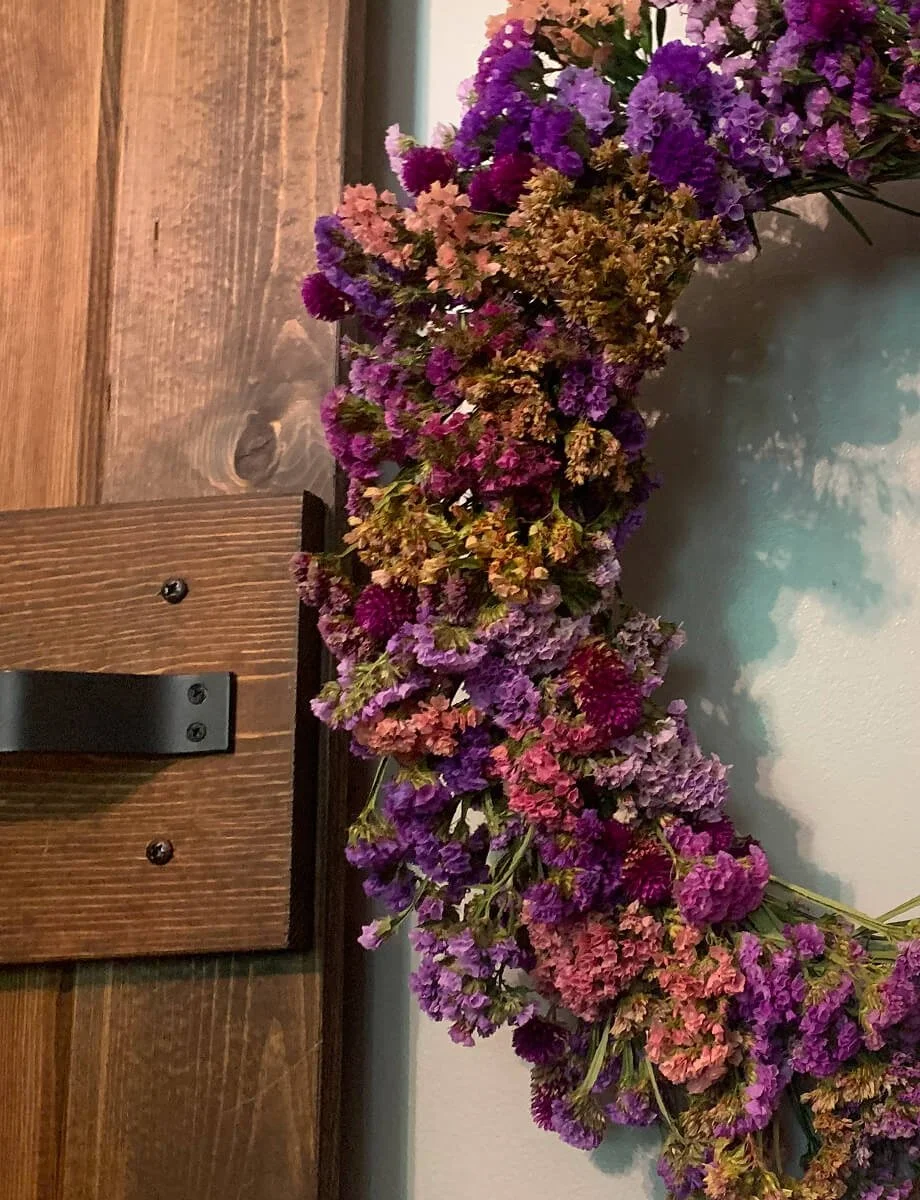 Handmade floral wreath made from dried flowers hanging on a wooden door.