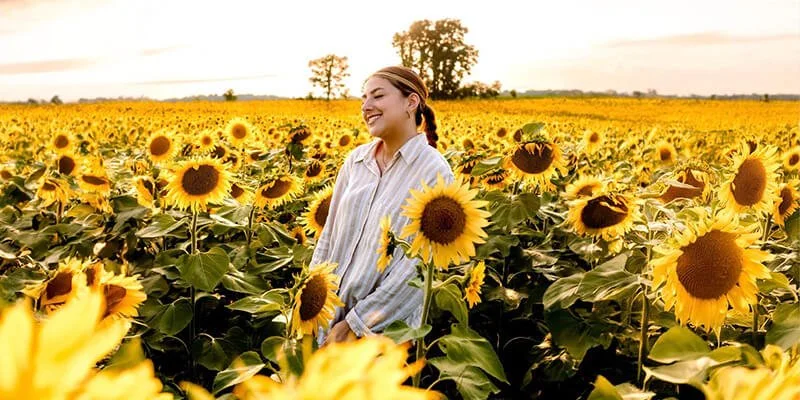 A woman standing in a large sunflower field, smiling and enjoying the sunny day.