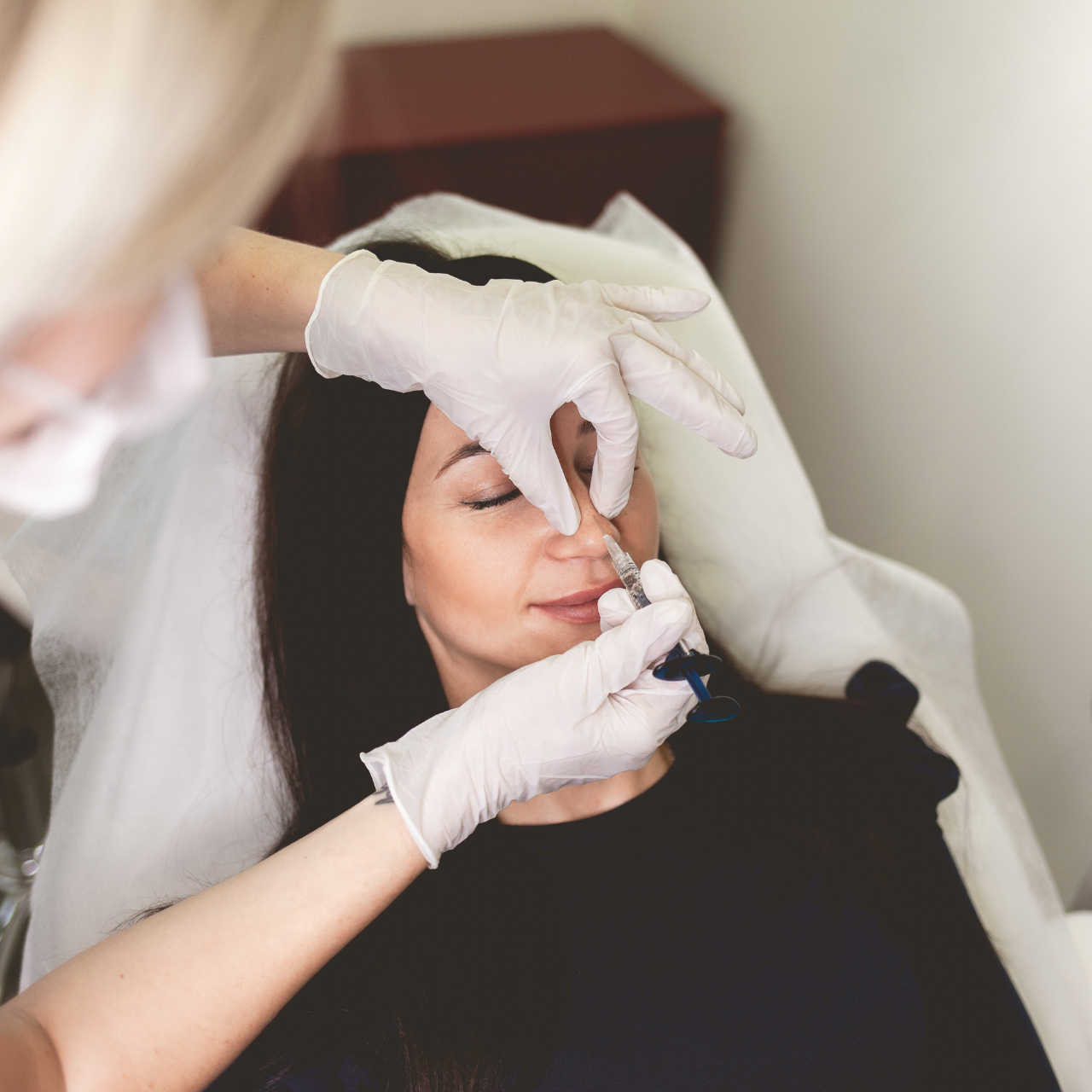 Una donna riceve un'iniezione sotto il sopracciglio mentre giace distesa su una poltrona reclinabile con un tutore per la testa, in un ambiente clinico.